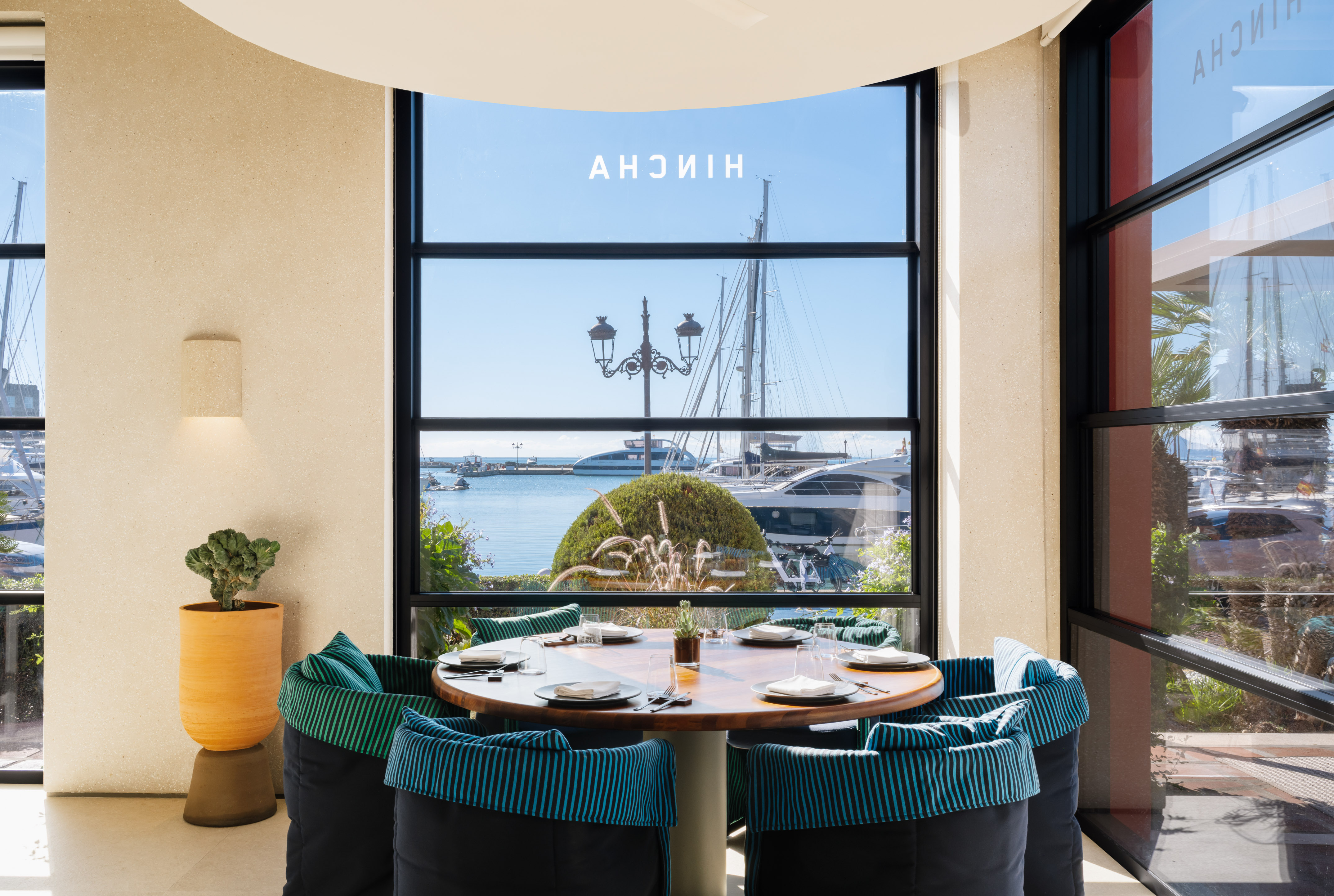 Modern restaurant with marina view, round table, and striped chairs.