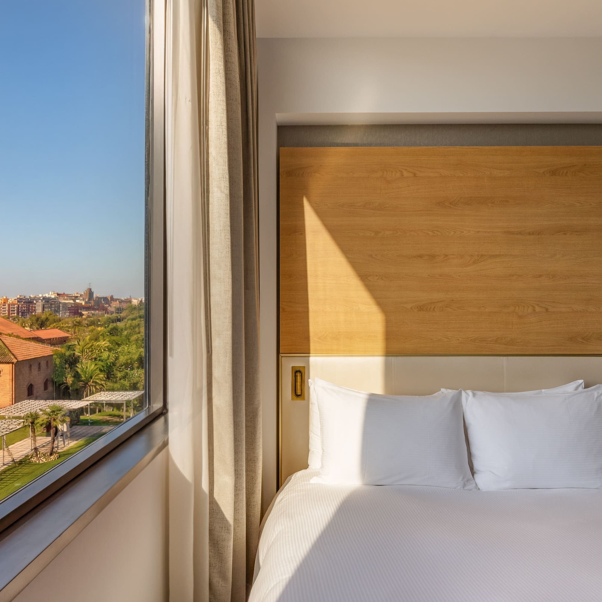 Modern hotel room with comfortable bed and scenic city garden view.