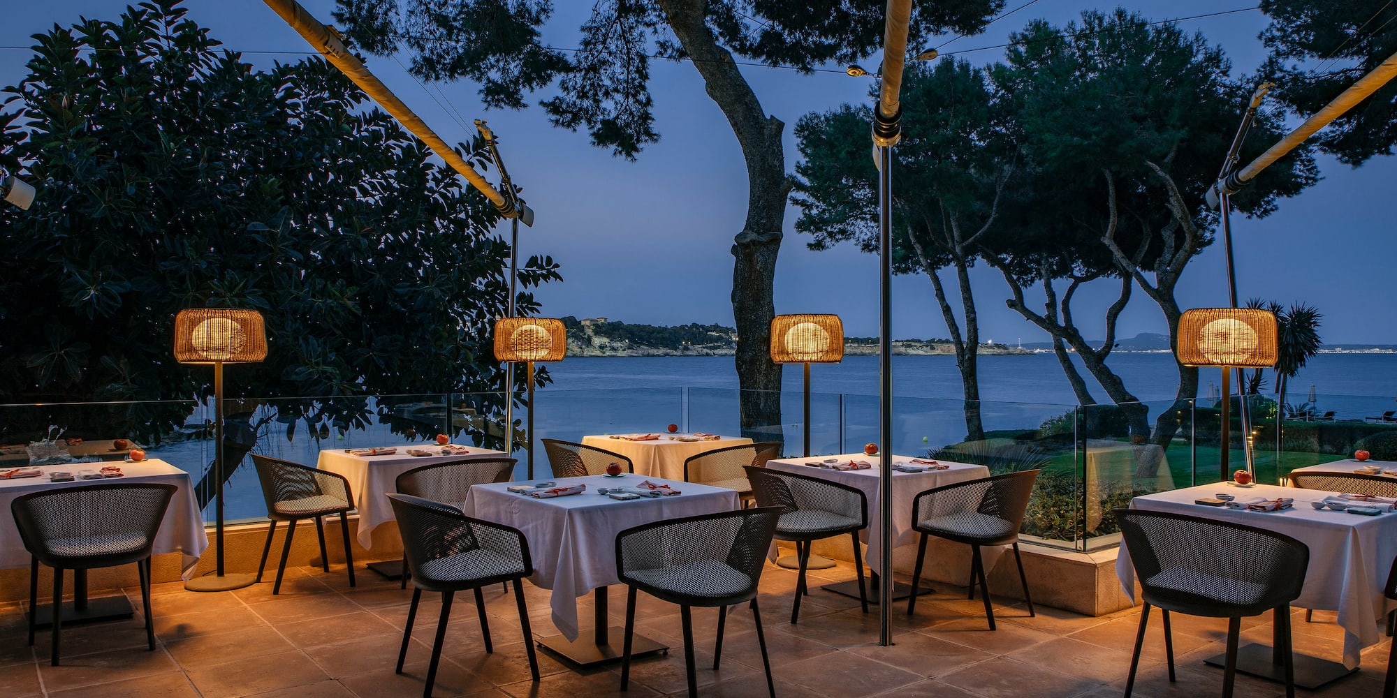 a table and chairs outside with trees and water in the background