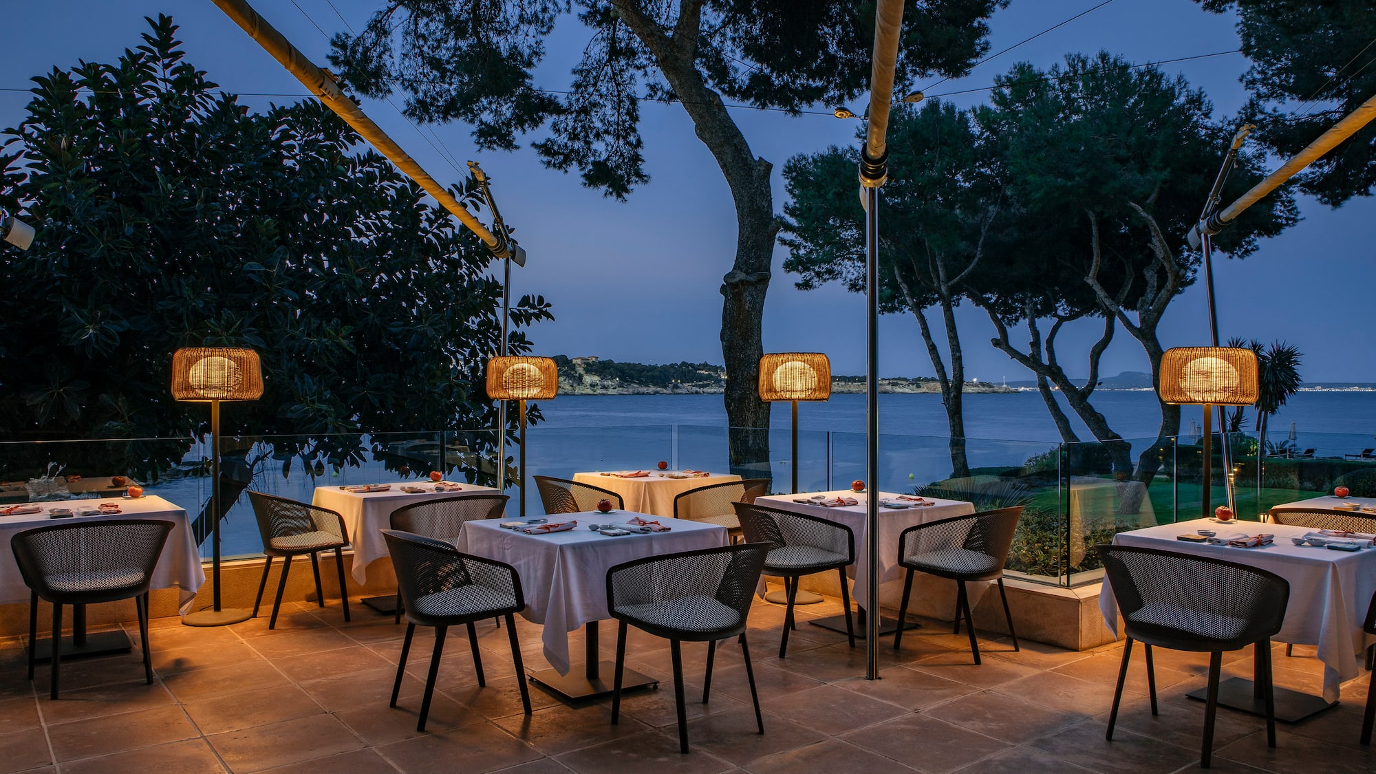 a table and chairs outside with trees and water in the background