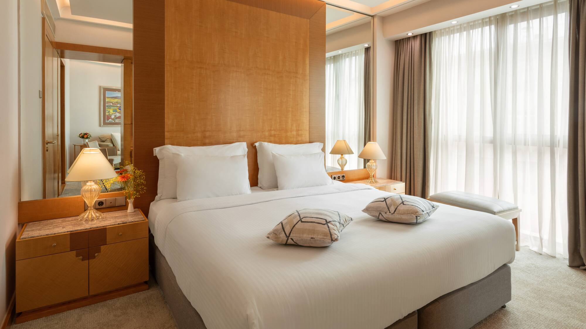 Luxury hotel bedroom with large bed, wooden headboard, and bright window.