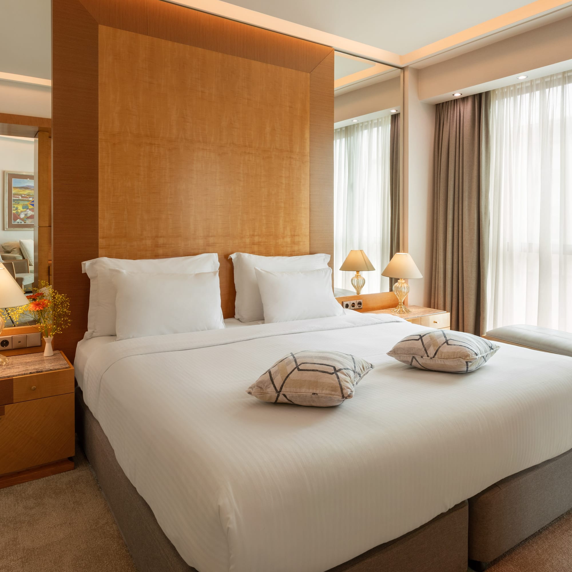 Luxury hotel bedroom with large bed, wooden headboard, and bright window.