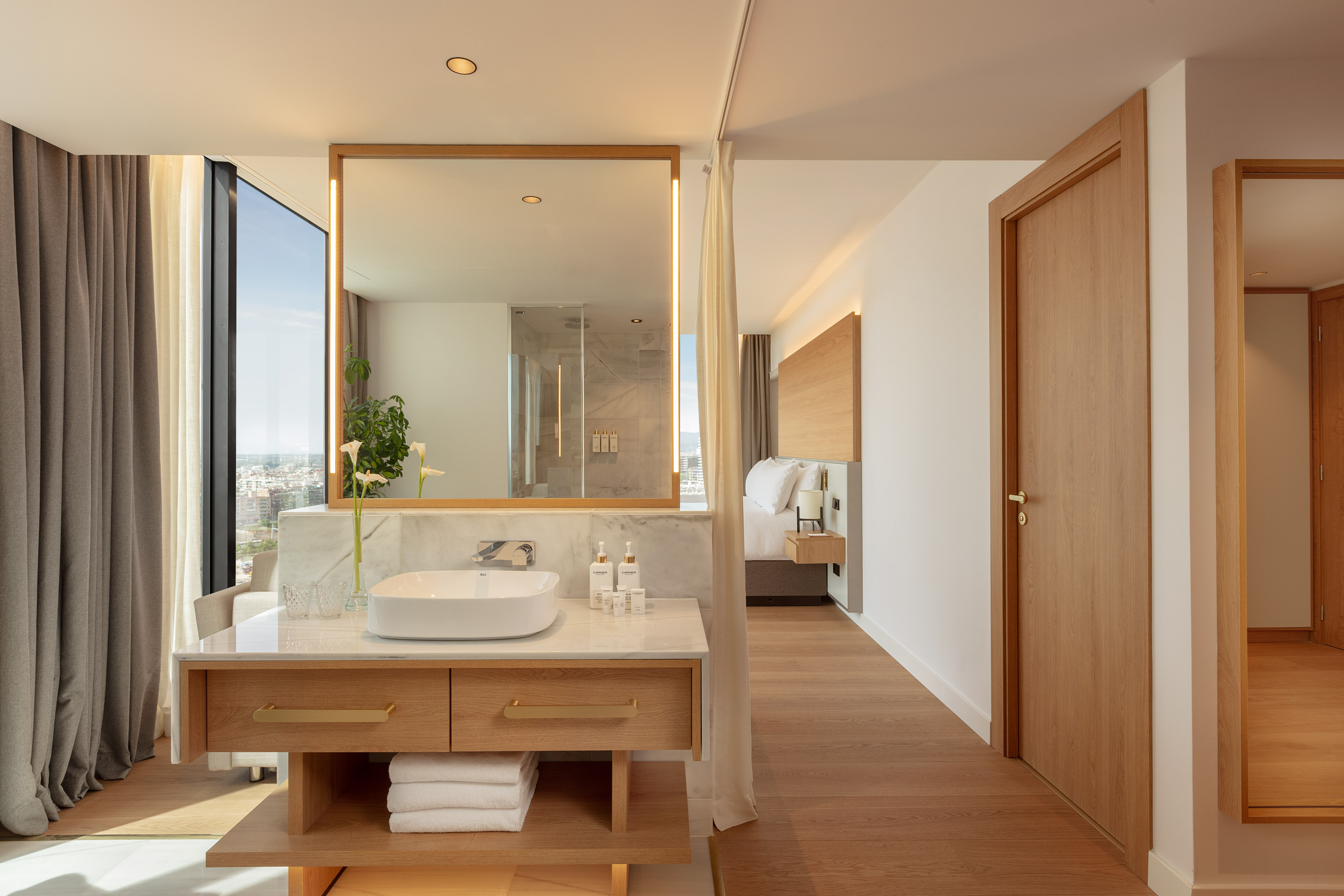 Modern hotel bathroom vanity with city view, connected to a bedroom.