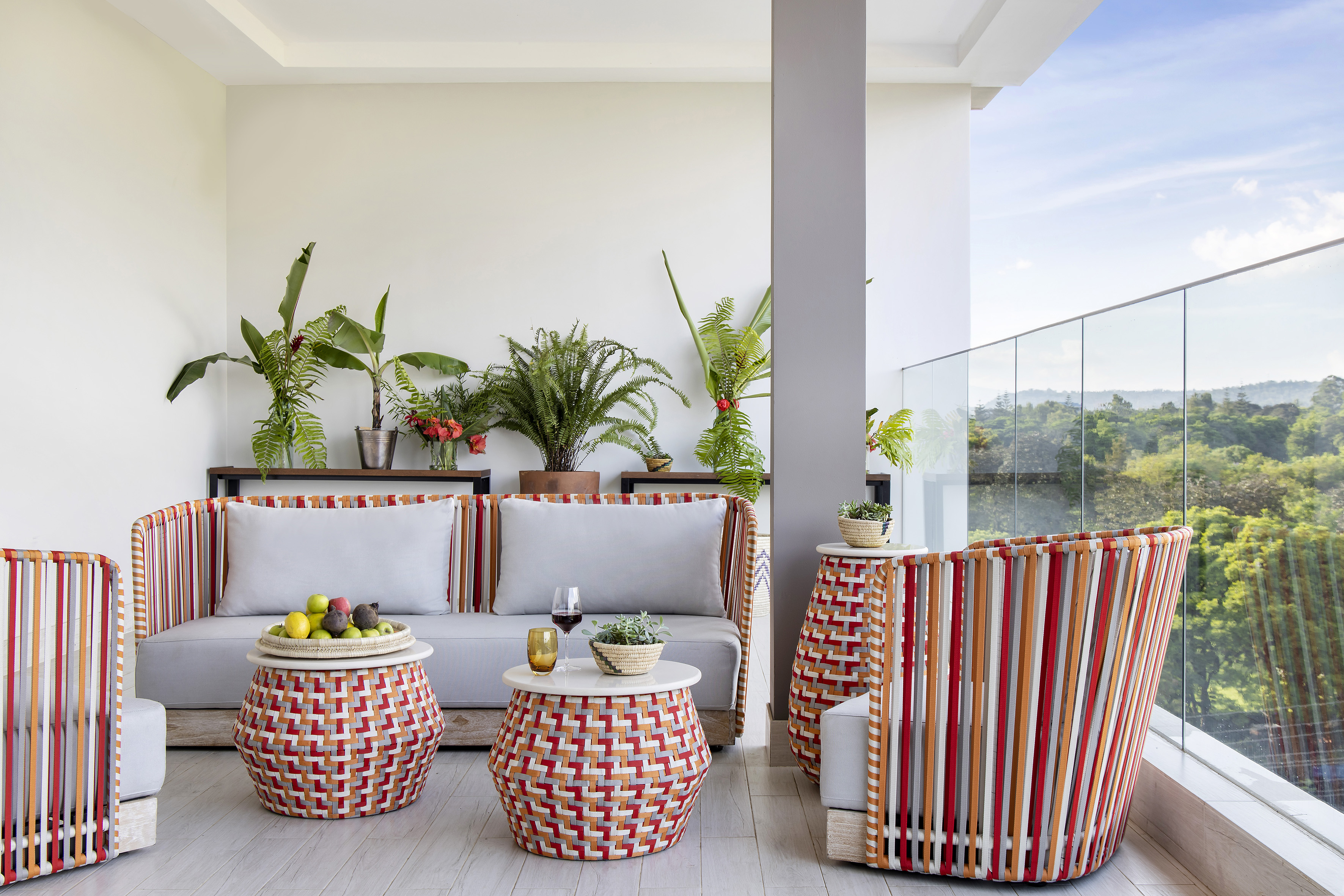 Balcony with colorful woven outdoor furniture, tropical plants, and forest view.