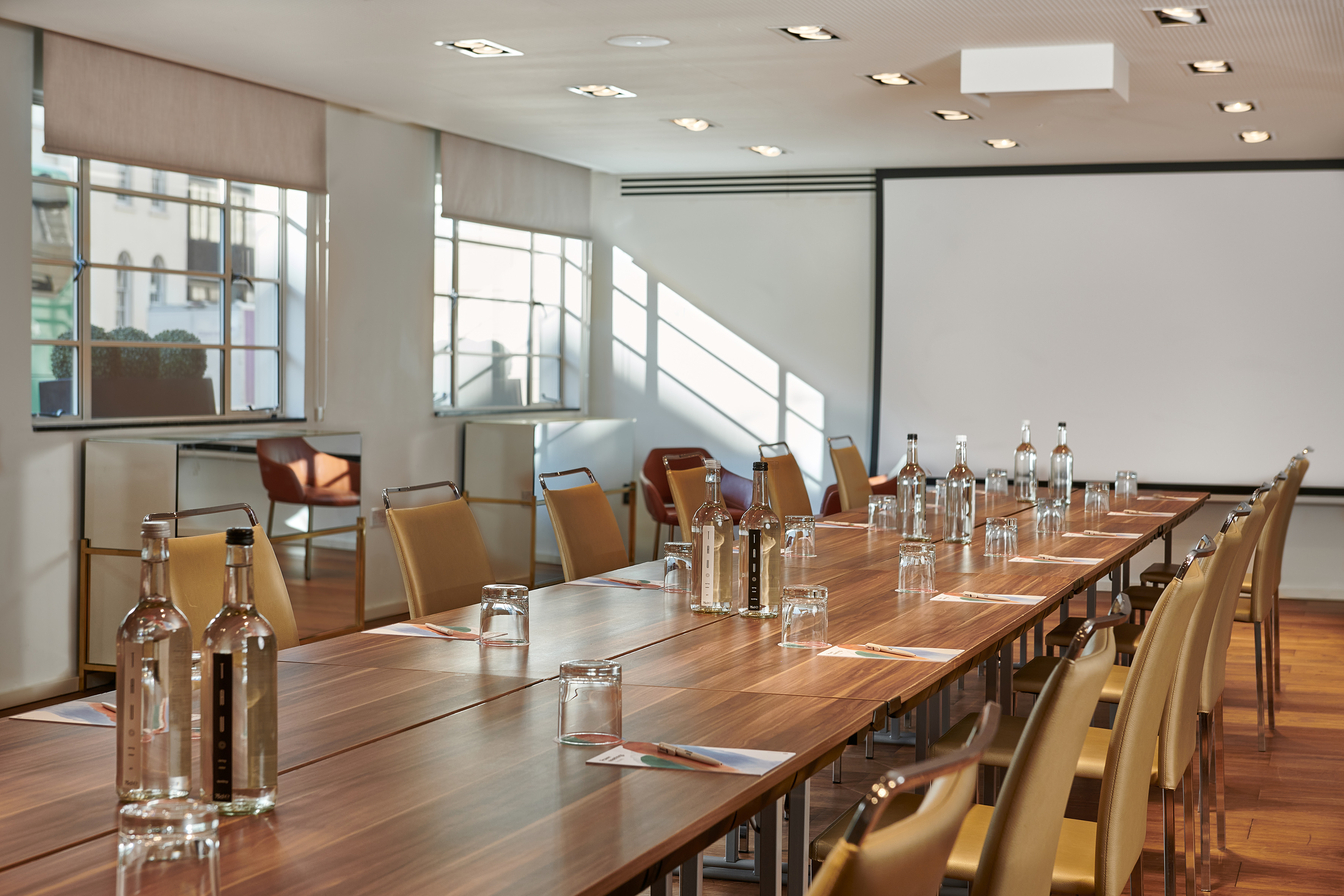 Modern conference room with long table, chairs, water bottles, and projector screen.