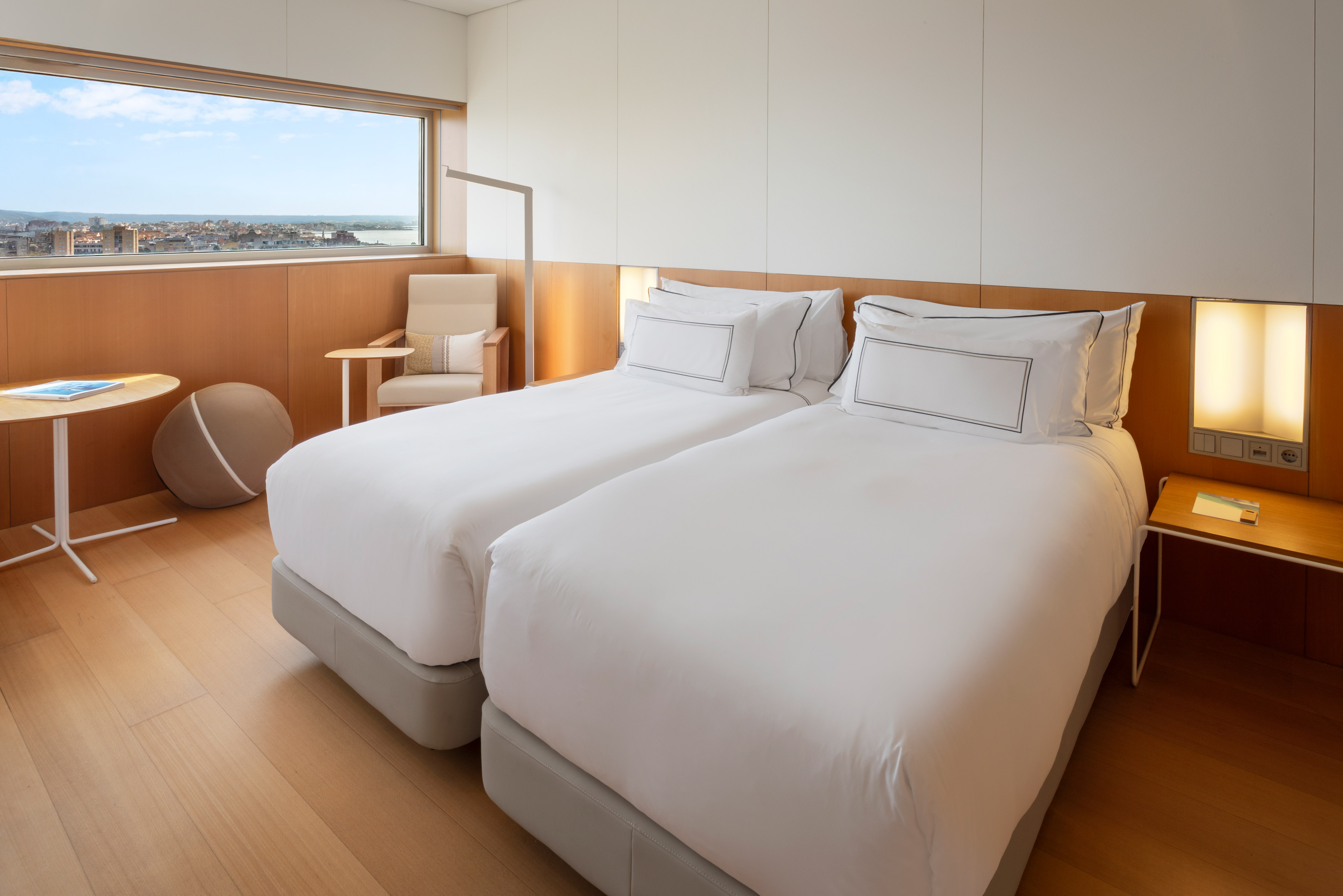 Modern hotel twin room with city view, white beds, and wood accents.