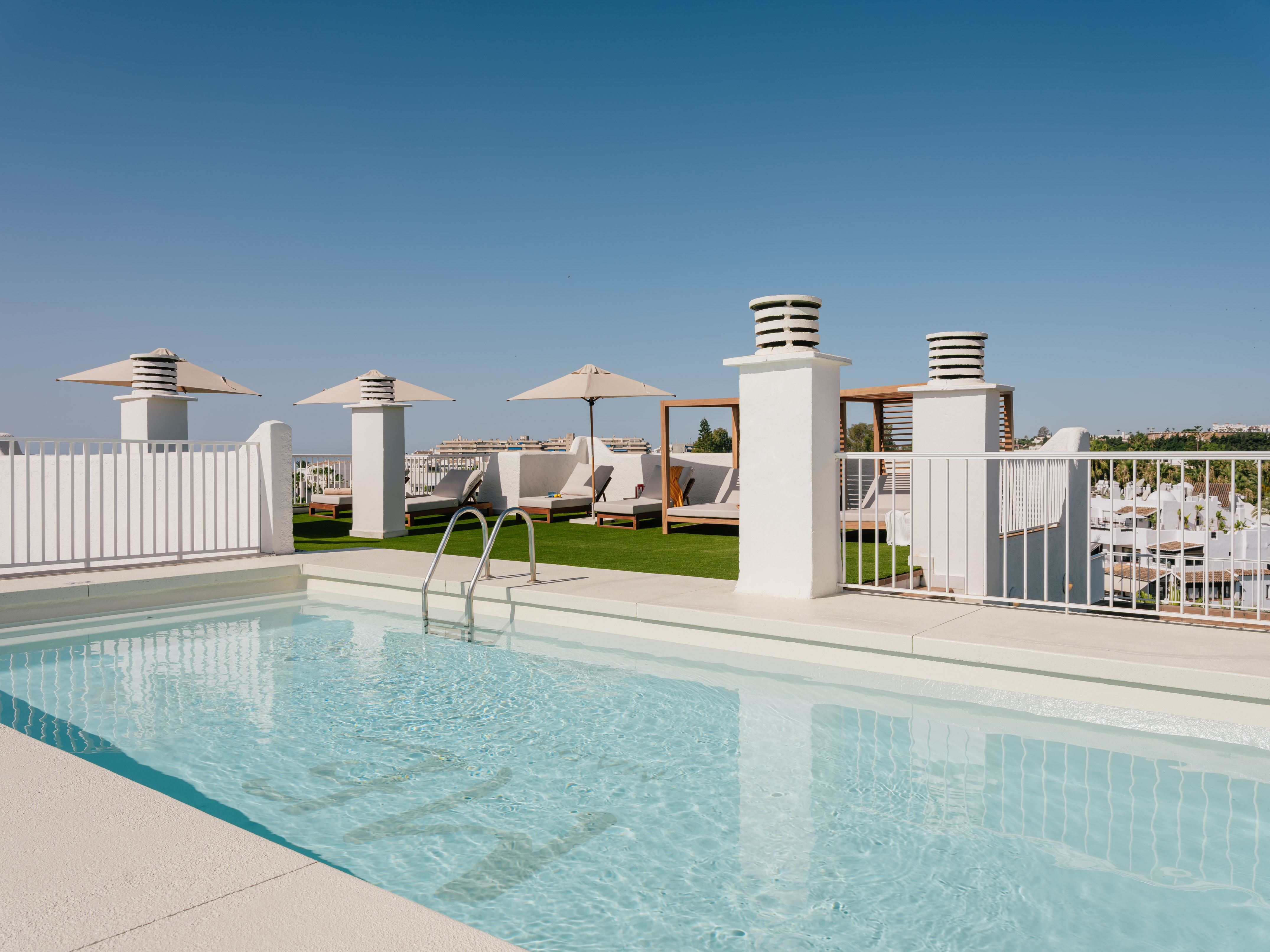 Resort rooftop pool with white architecture, sun loungers, and clear blue sky.