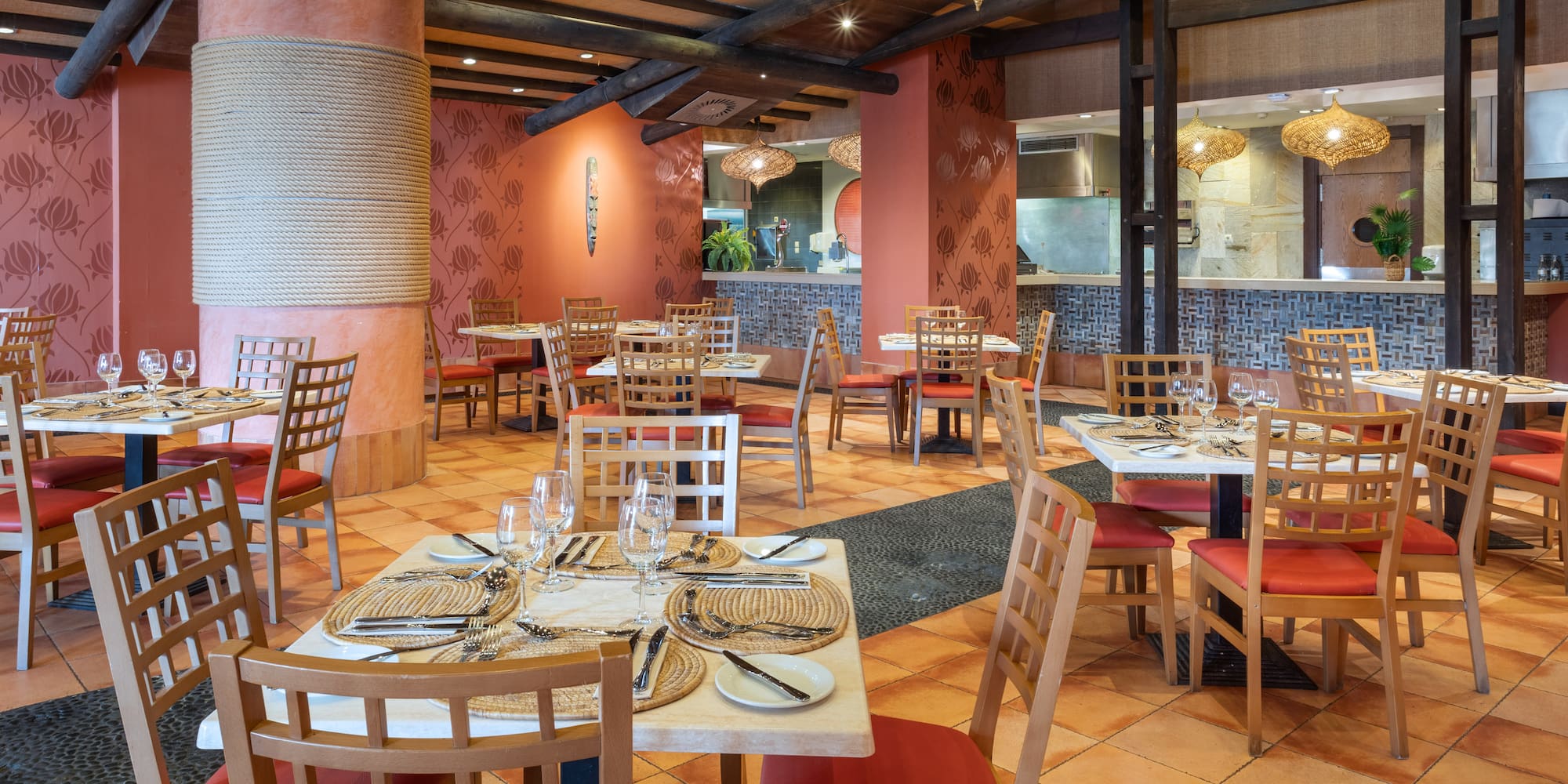 Tropical restaurant interior with red chairs, set tables, and terracotta floor.