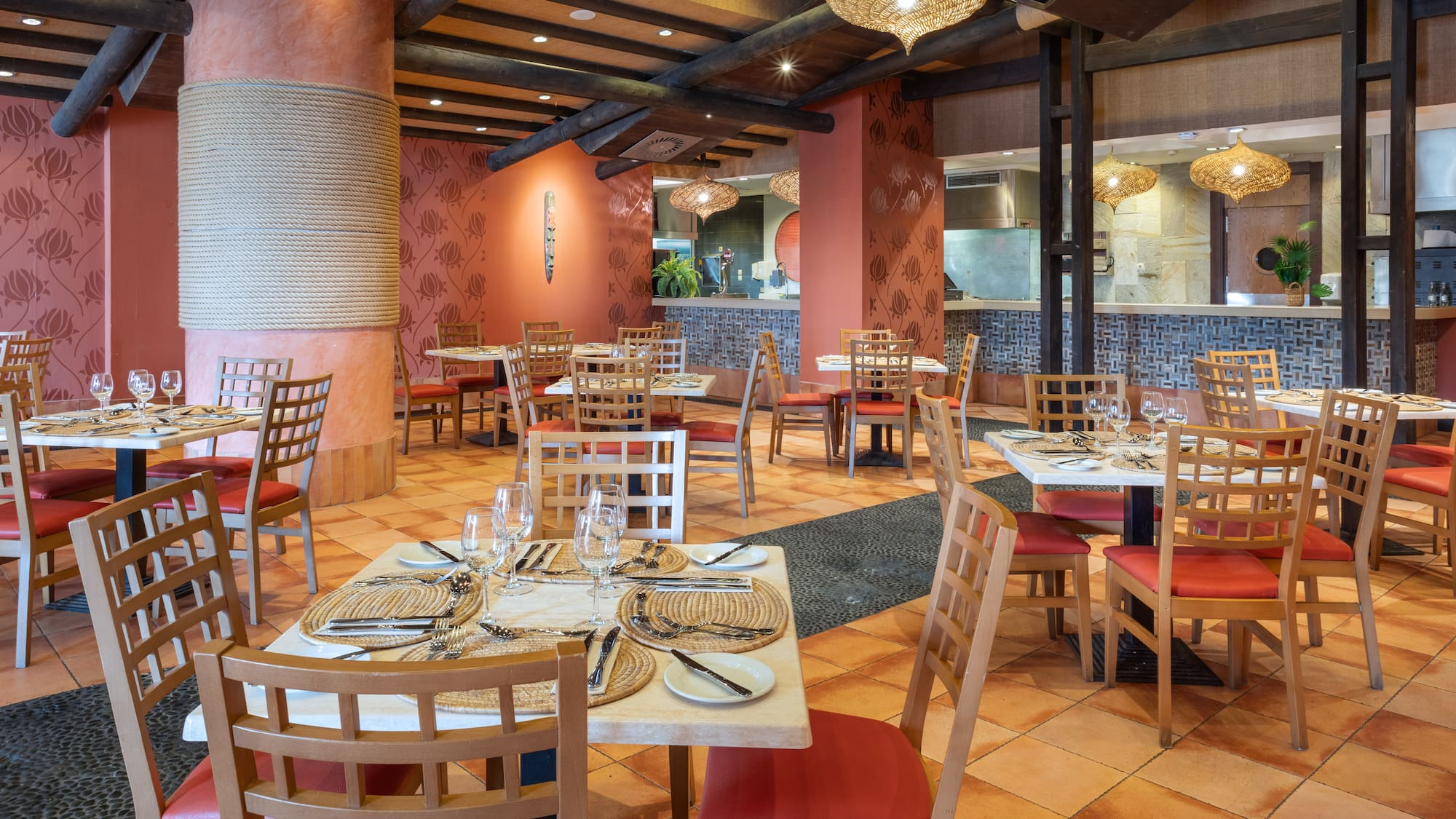 Tropical restaurant interior with red chairs, set tables, and terracotta floor.