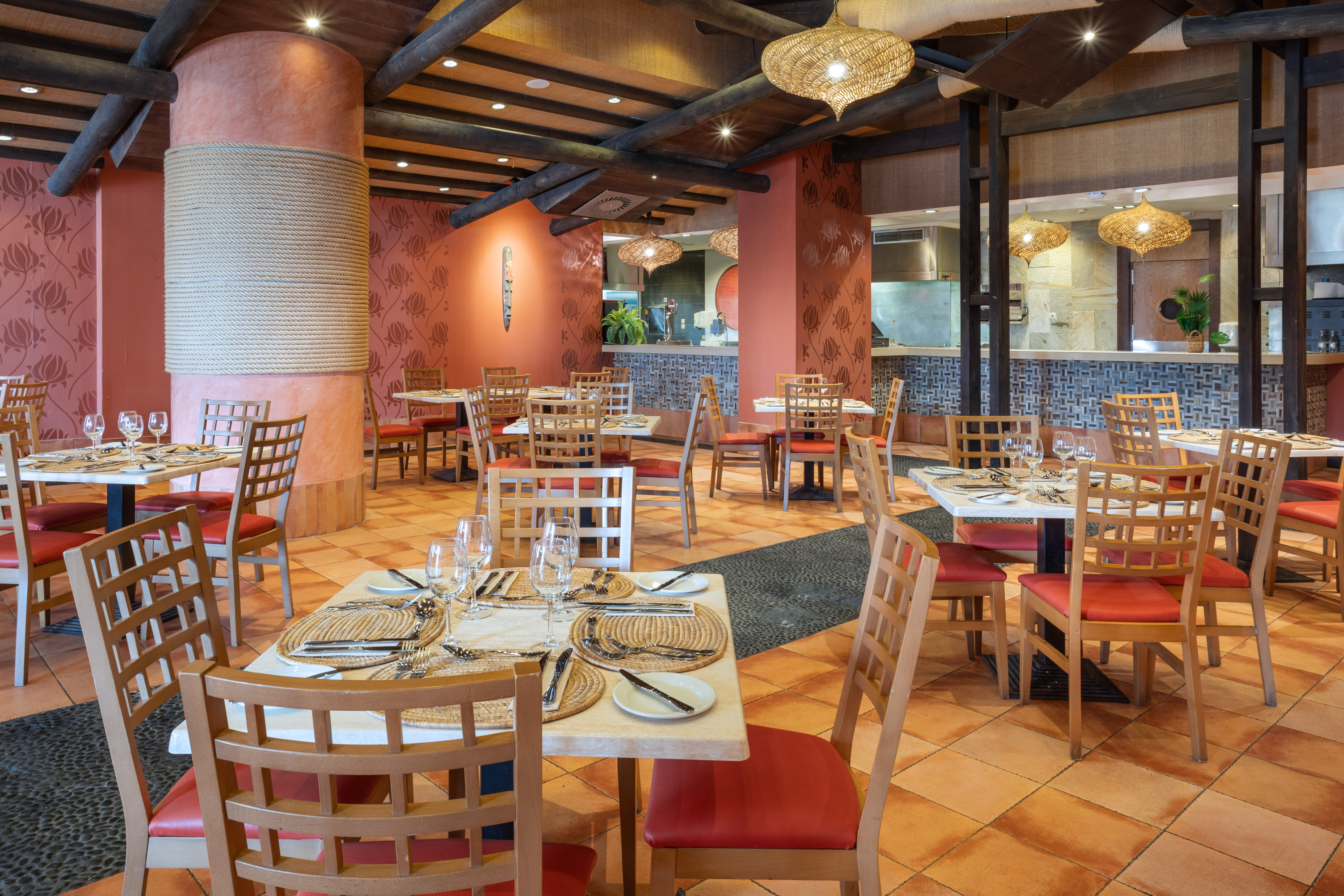Tropical restaurant interior with red chairs, set tables, and terracotta floor.
