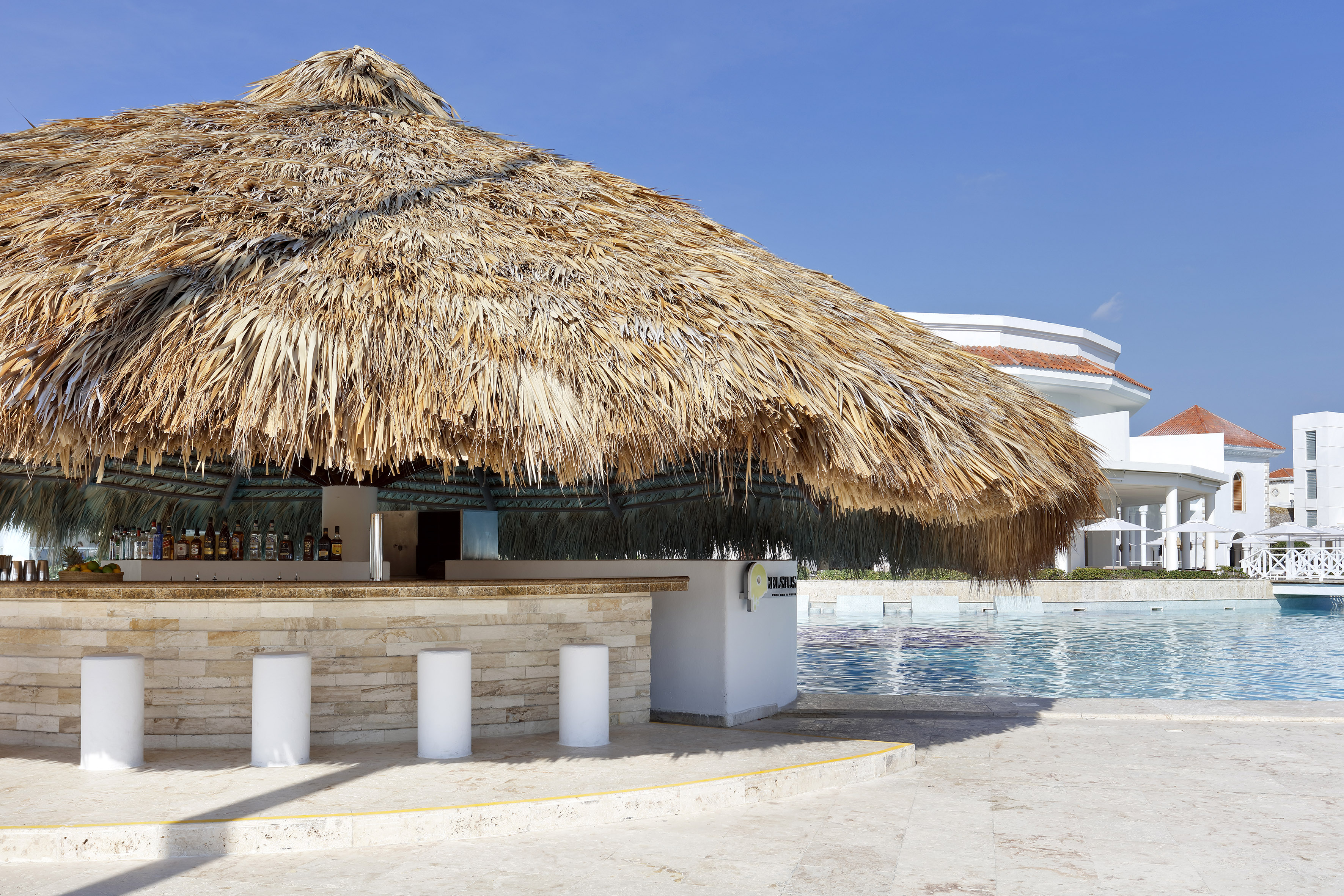 Resort swim-up bar with thatched roof by blue pool.