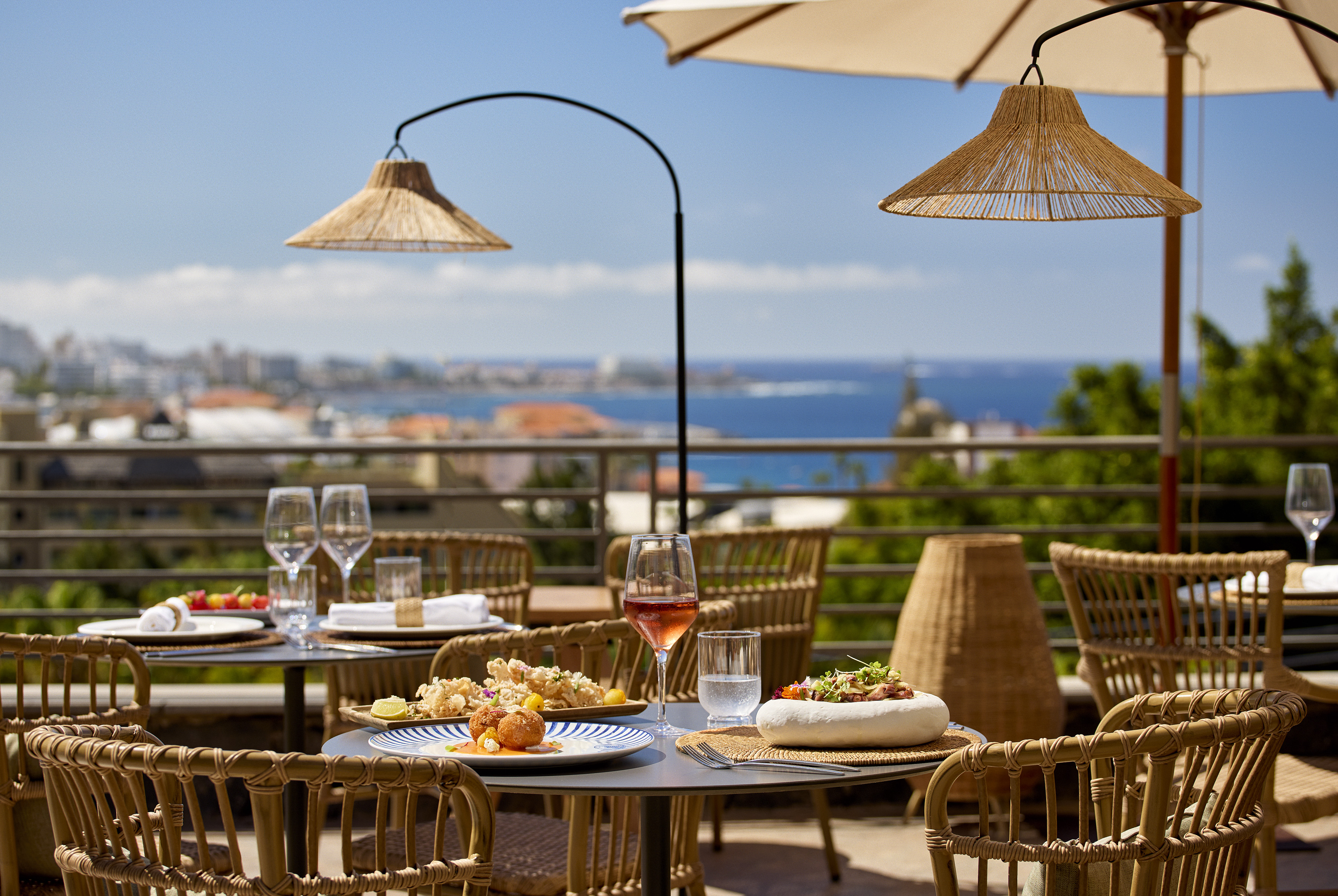 Al fresco restaurant terrace with gourmet dishes, rattan decor, and sea view.