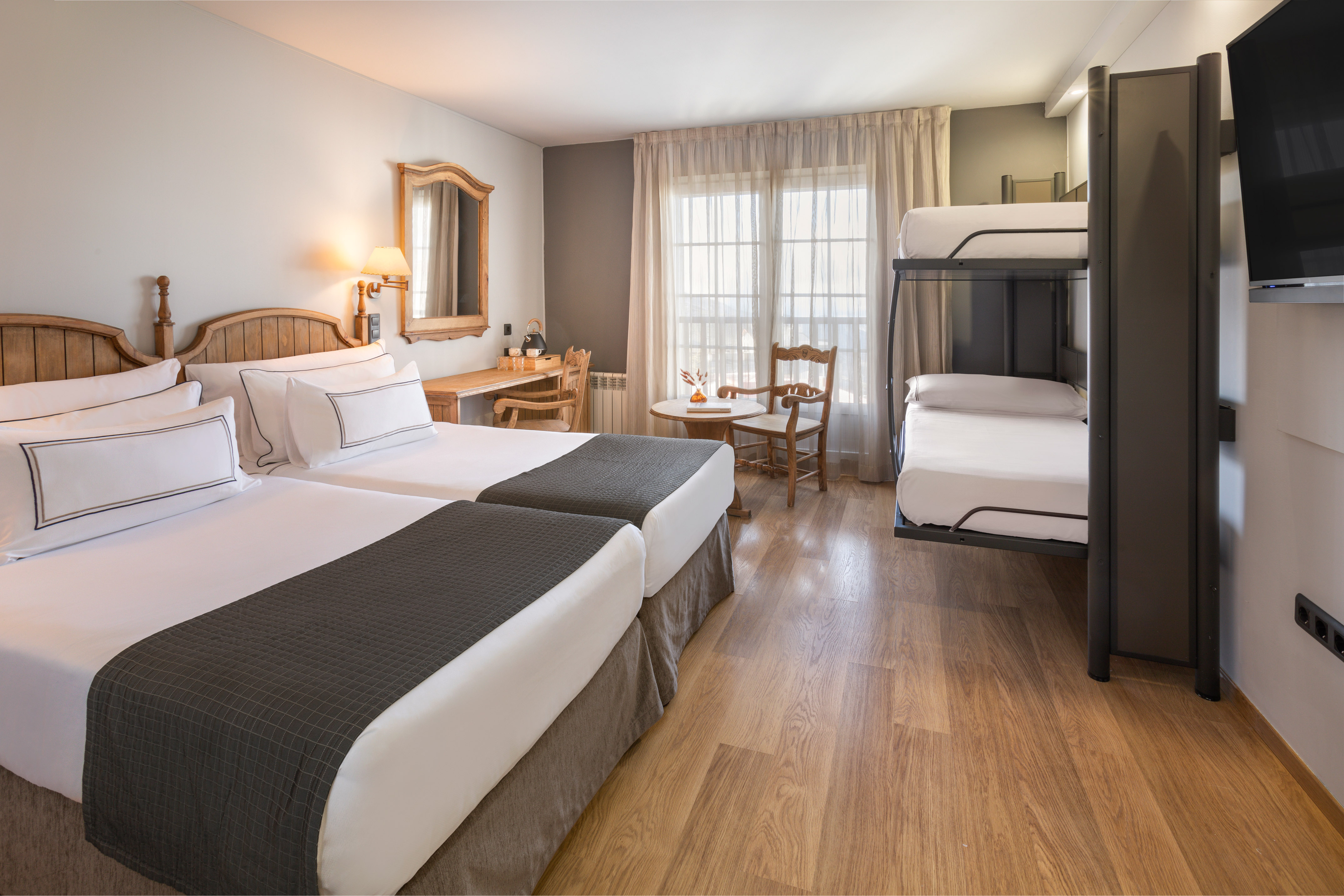 Spacious hotel room with twin beds, bunk bed, desk, and rustic decor.