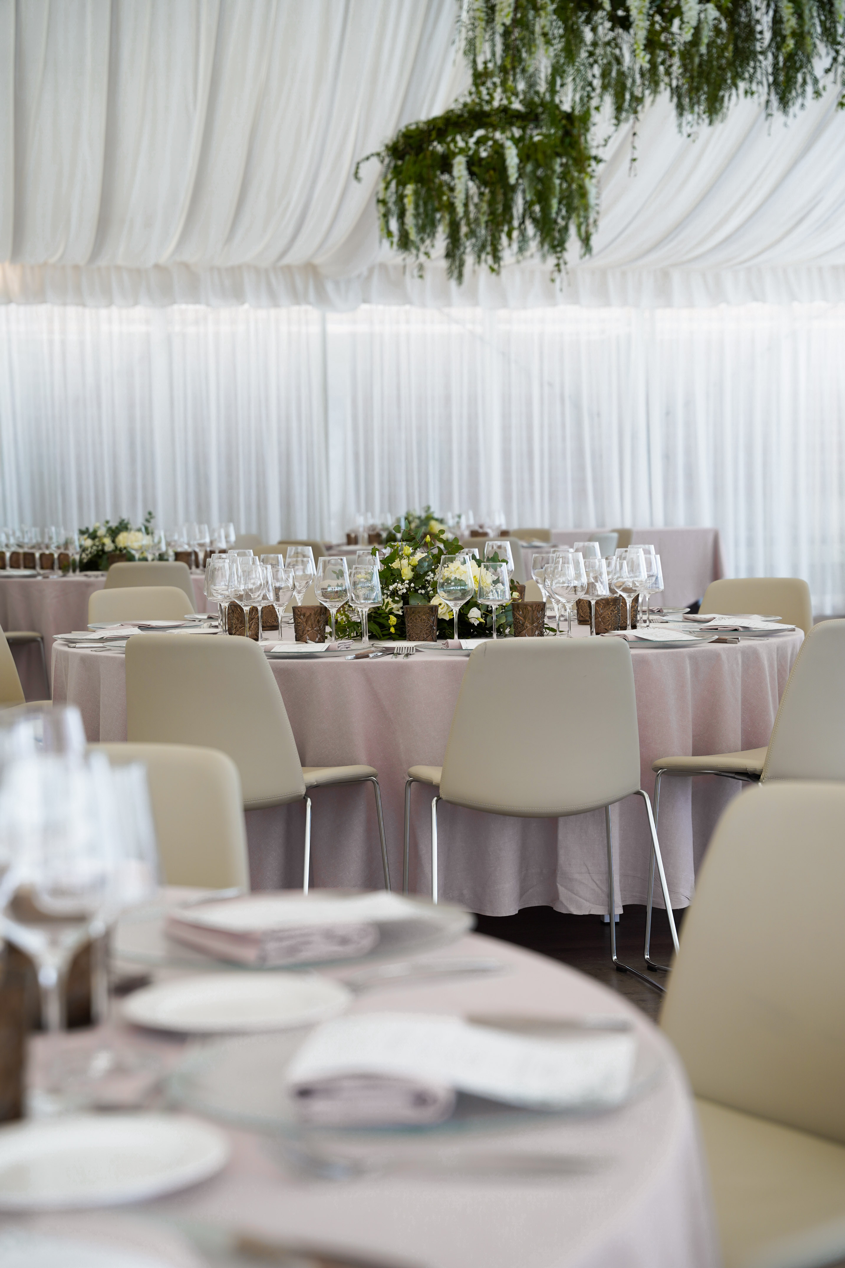 Wedding reception tables with pink linens, floral centerpieces, white drapes.
