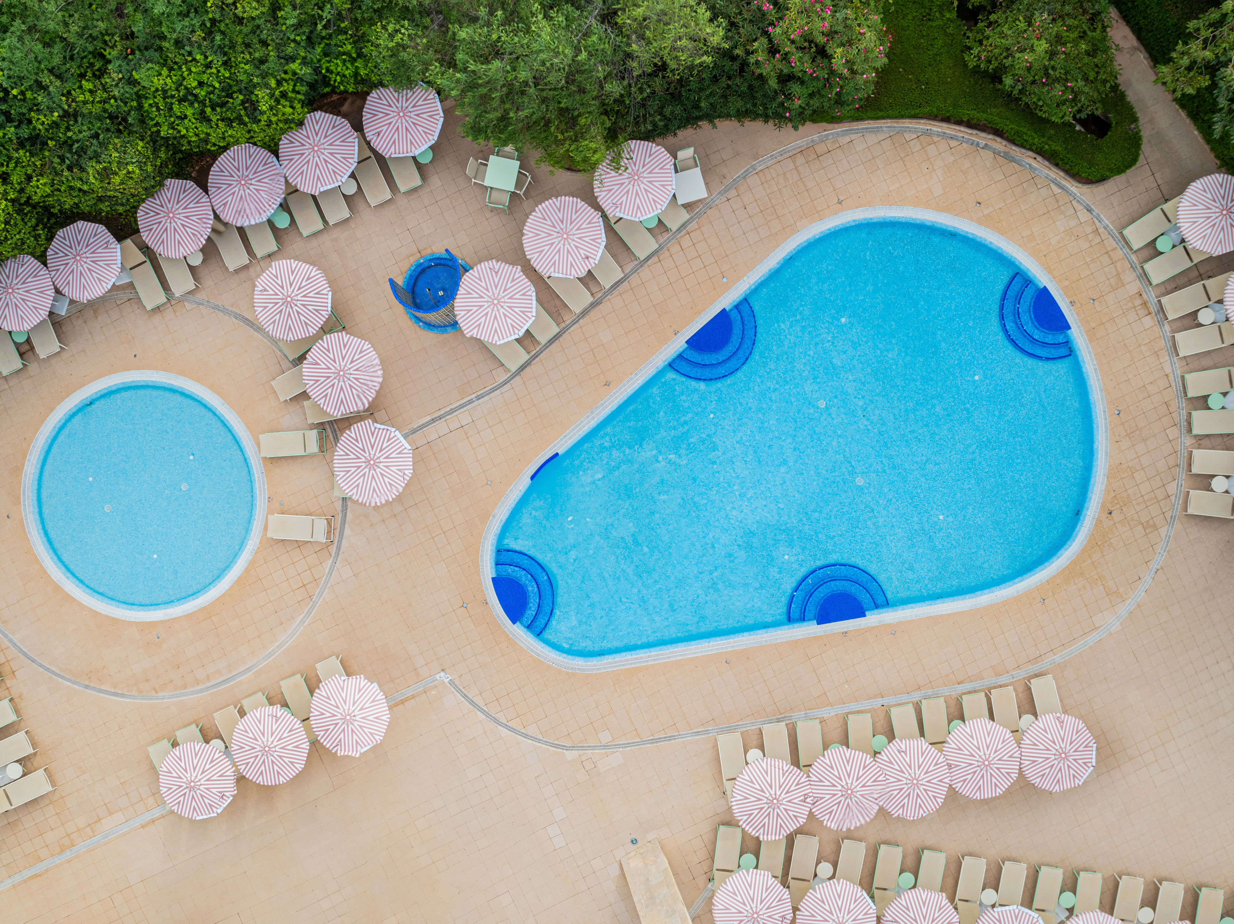 Aerial view of resort swimming pools, striped umbrellas, and lounge chairs on patio.