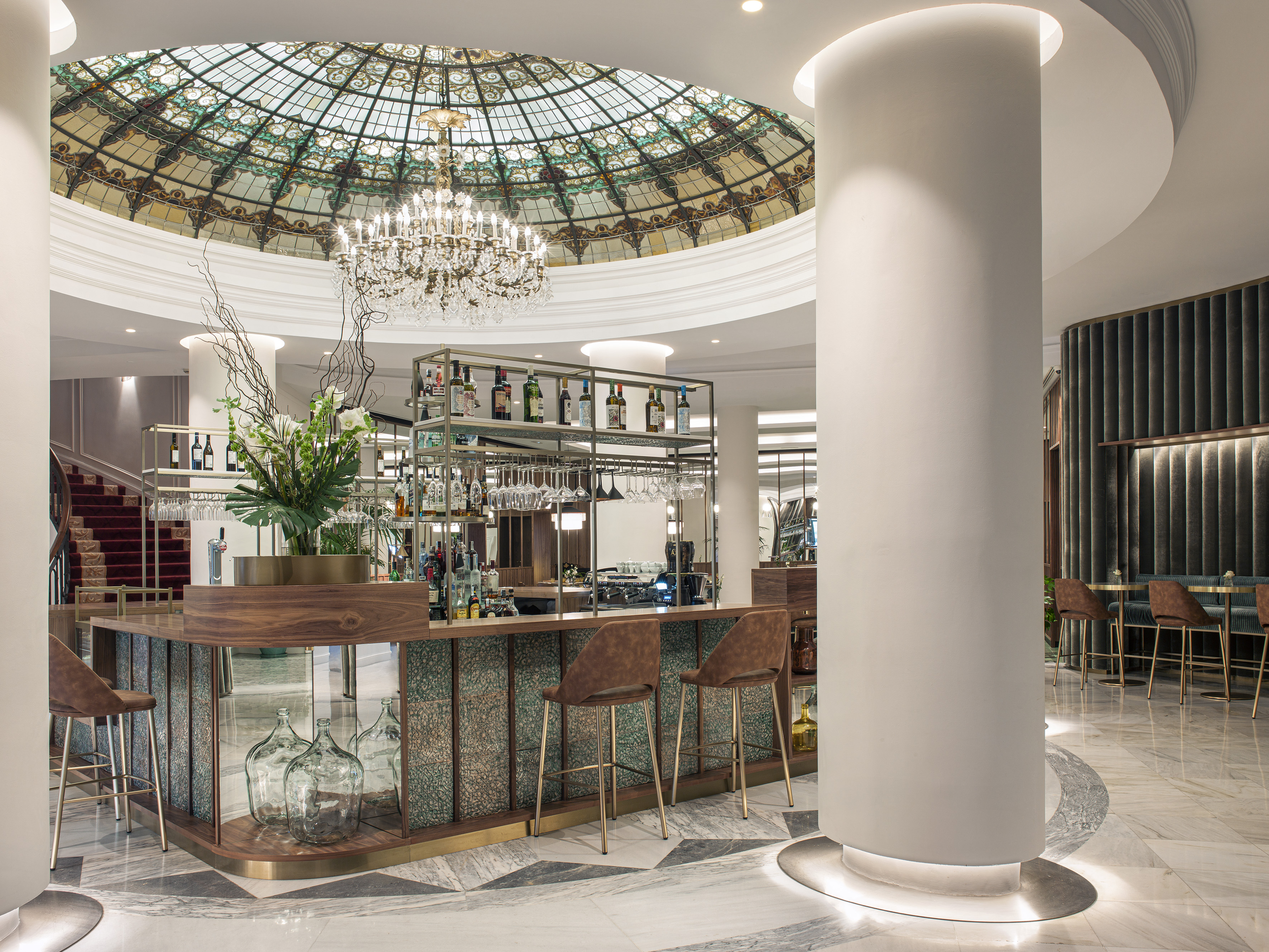 Hotel bar with stained glass dome, grand chandelier, and modern interior design.