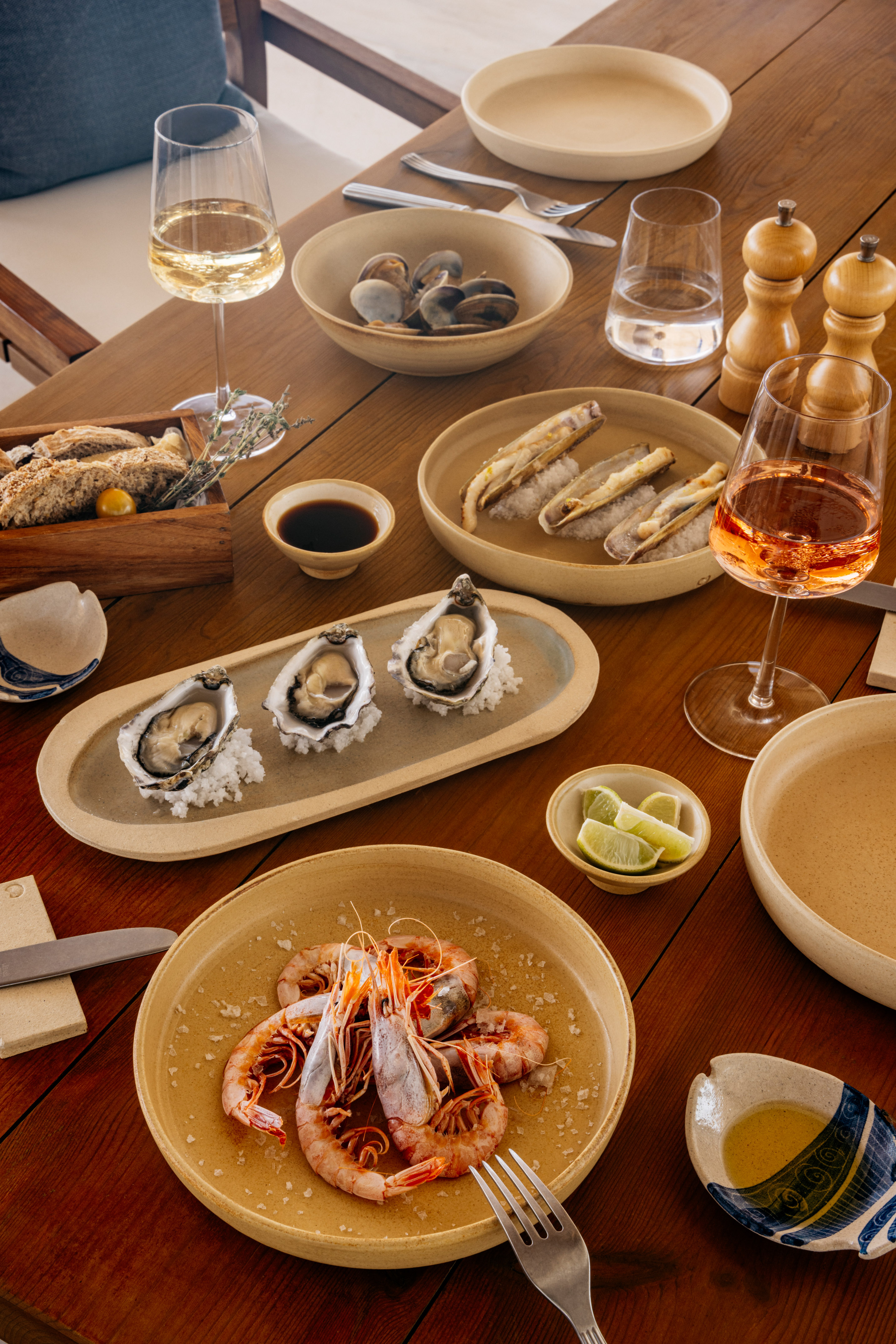 Gourmet seafood meal on a wooden table: oysters, prawns, clams, and wine.