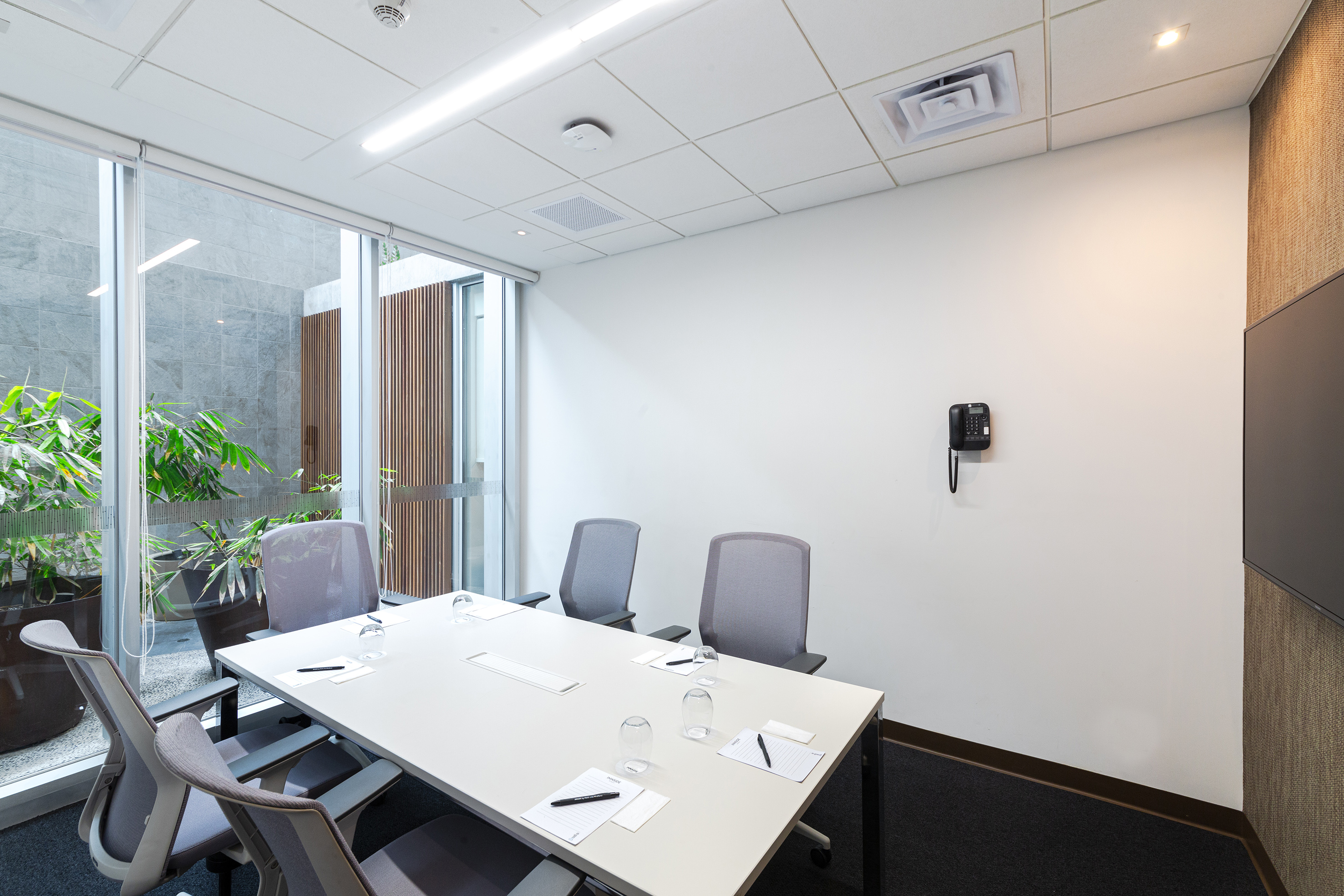 Modern conference room with long table, grey chairs, and a green outdoor garden.