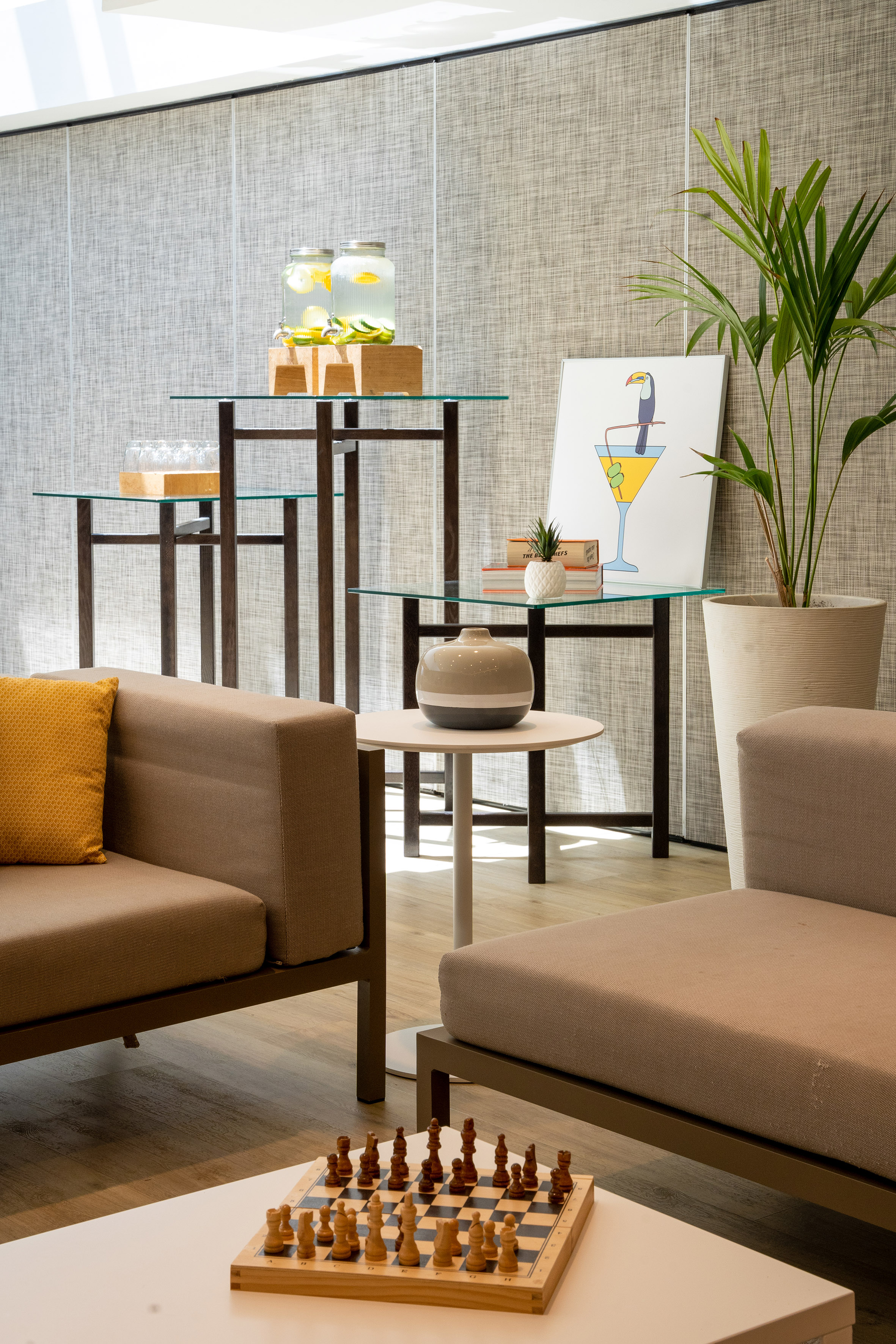 Modern lobby lounge with infused water, chessboard, comfy sofas, and tropical plant.