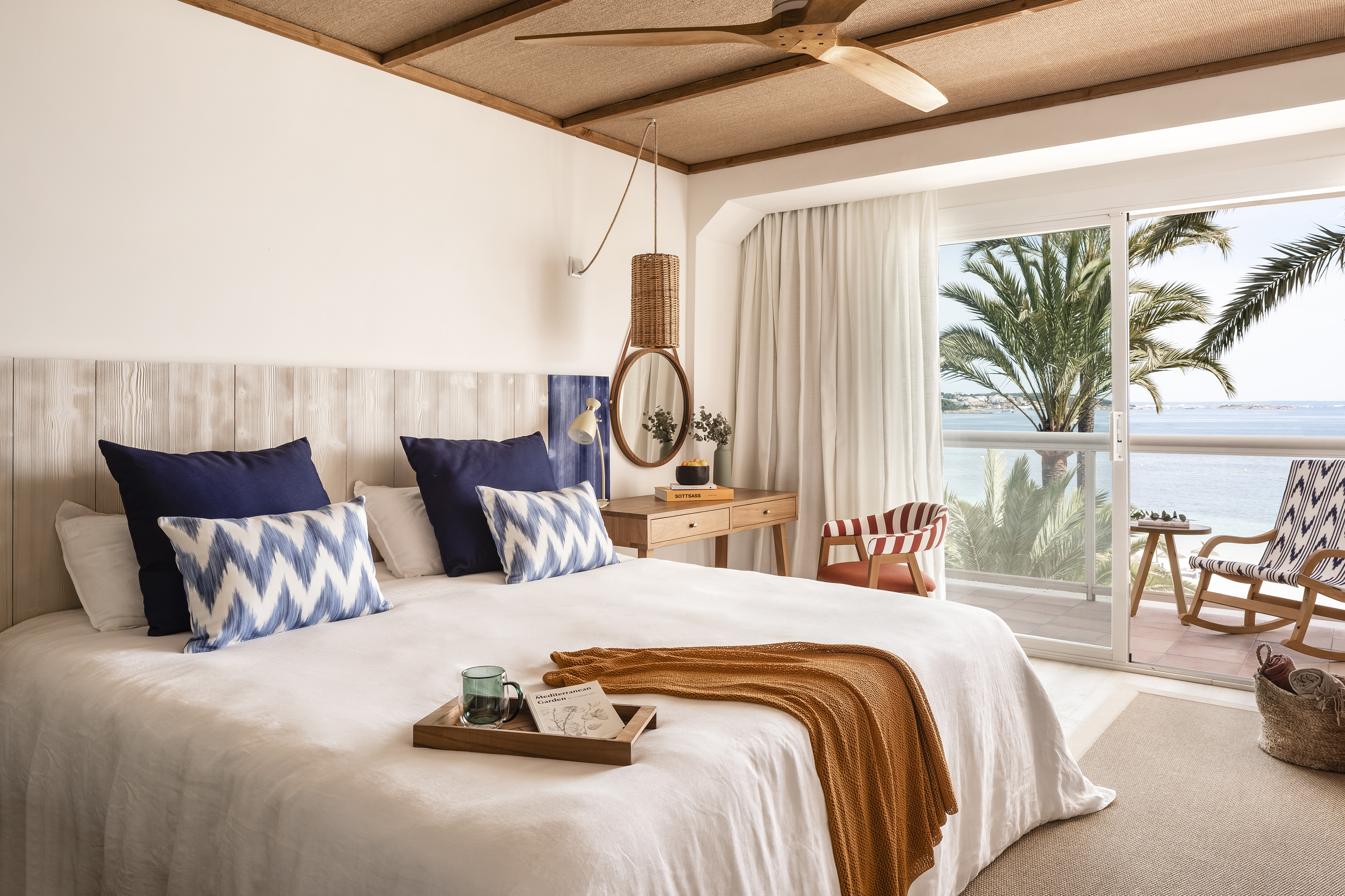 Coastal hotel bedroom with sea view, white bed, balcony, and natural wood.