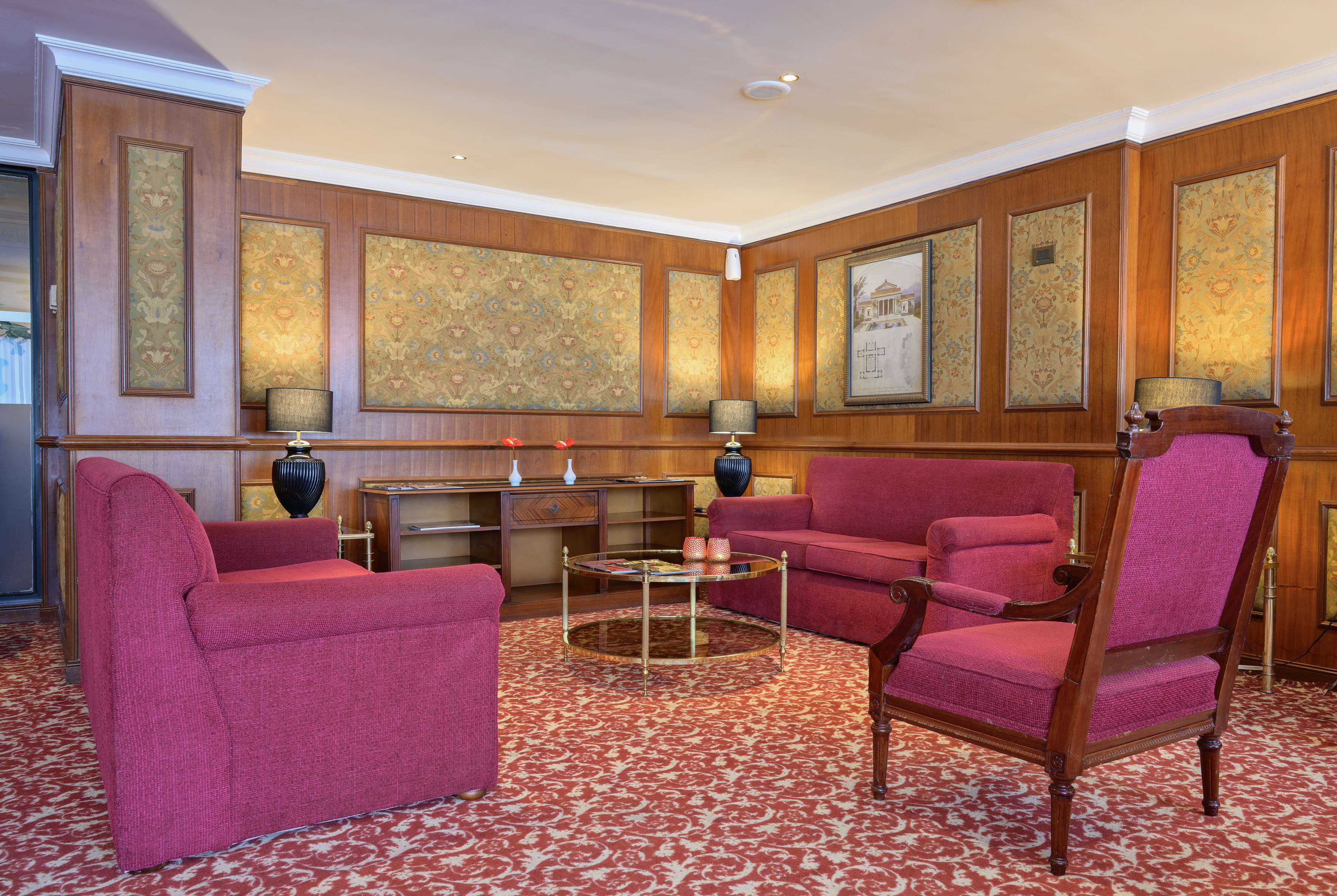 Elegant hotel lounge with red armchairs, wood paneling, and patterned carpet.