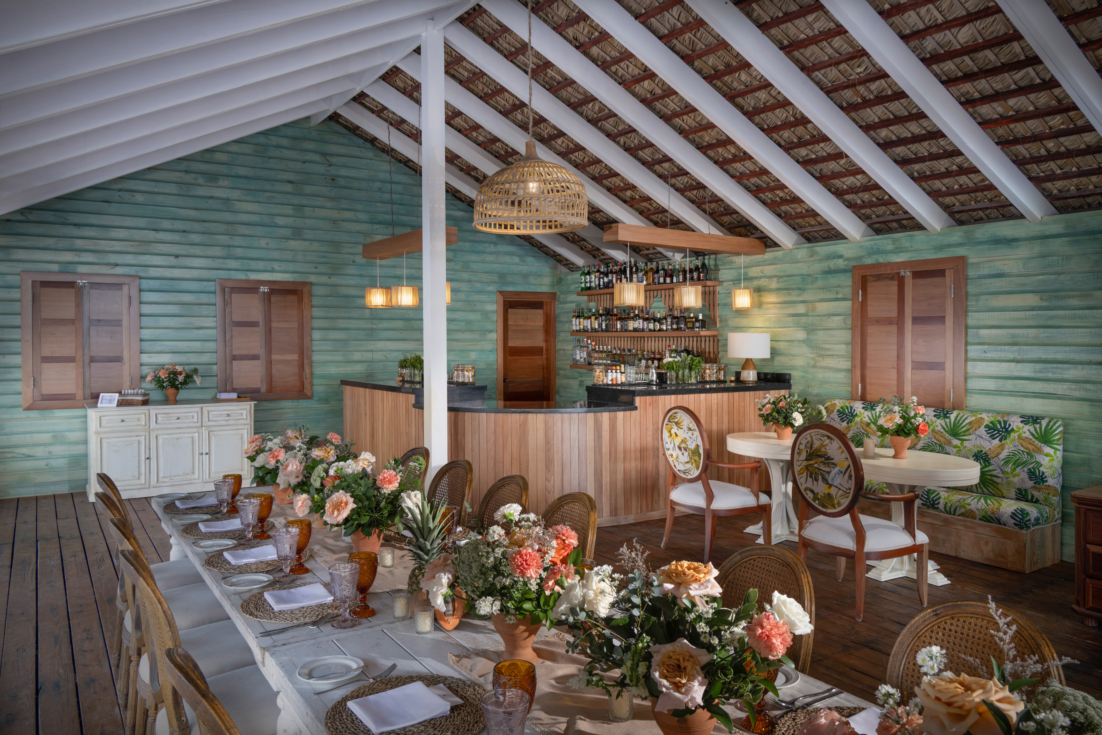 Tropical restaurant with set dining table, floral decor, and rustic wood bar.