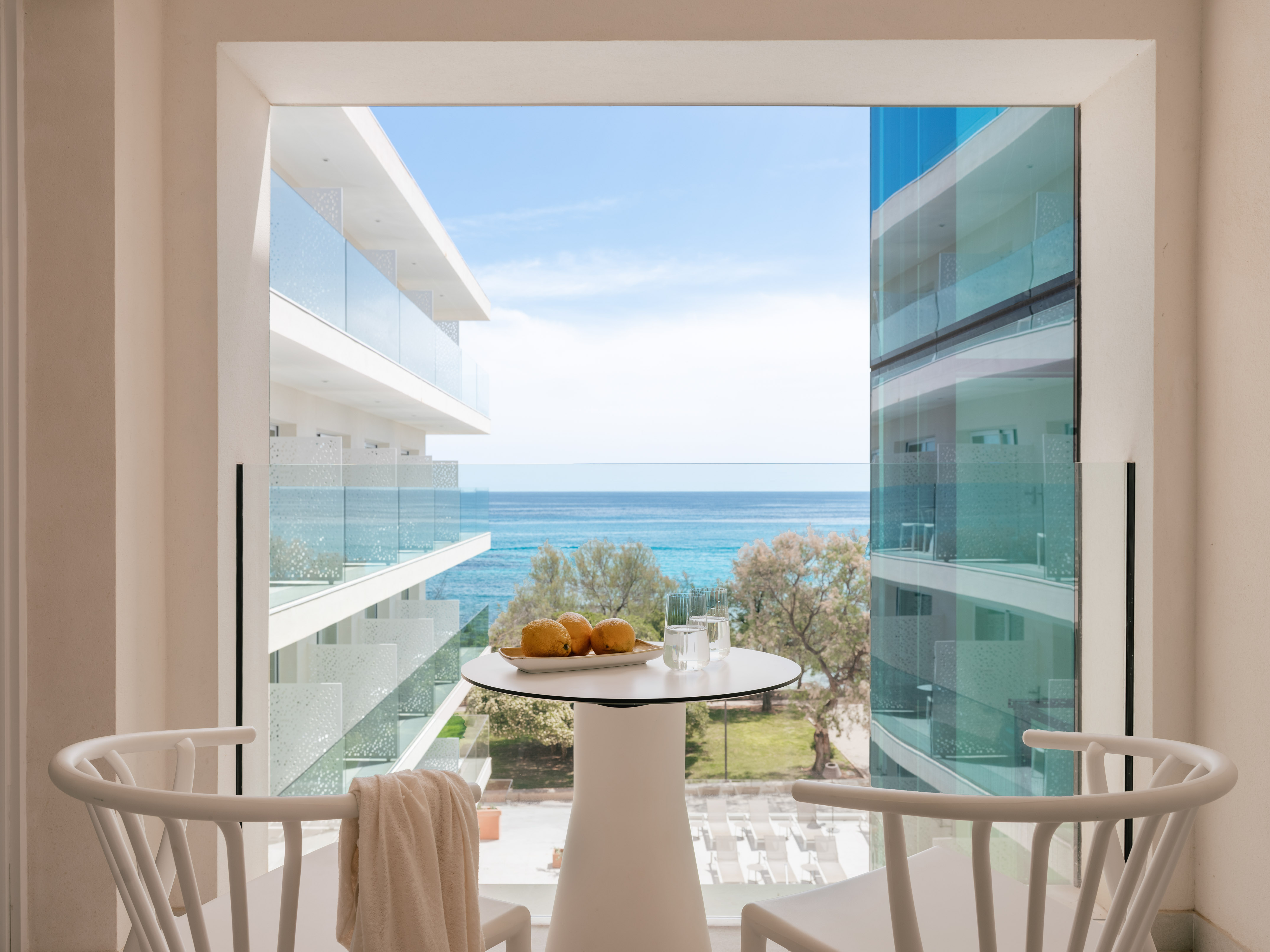 Modern hotel balcony with sea view, white table with lemons, and chairs.