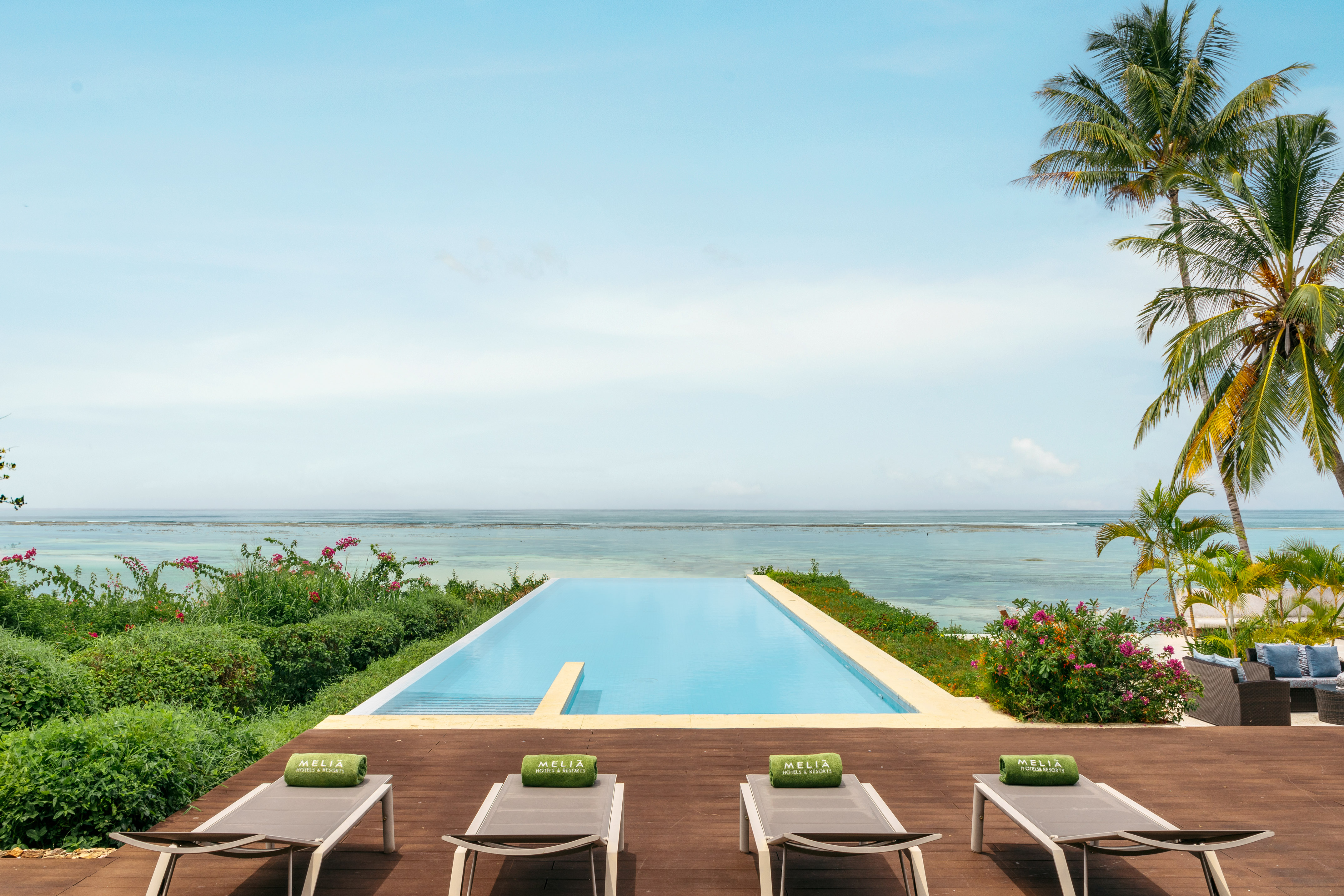 Meliá resort infinity pool with ocean view, sun loungers, and palm trees.
