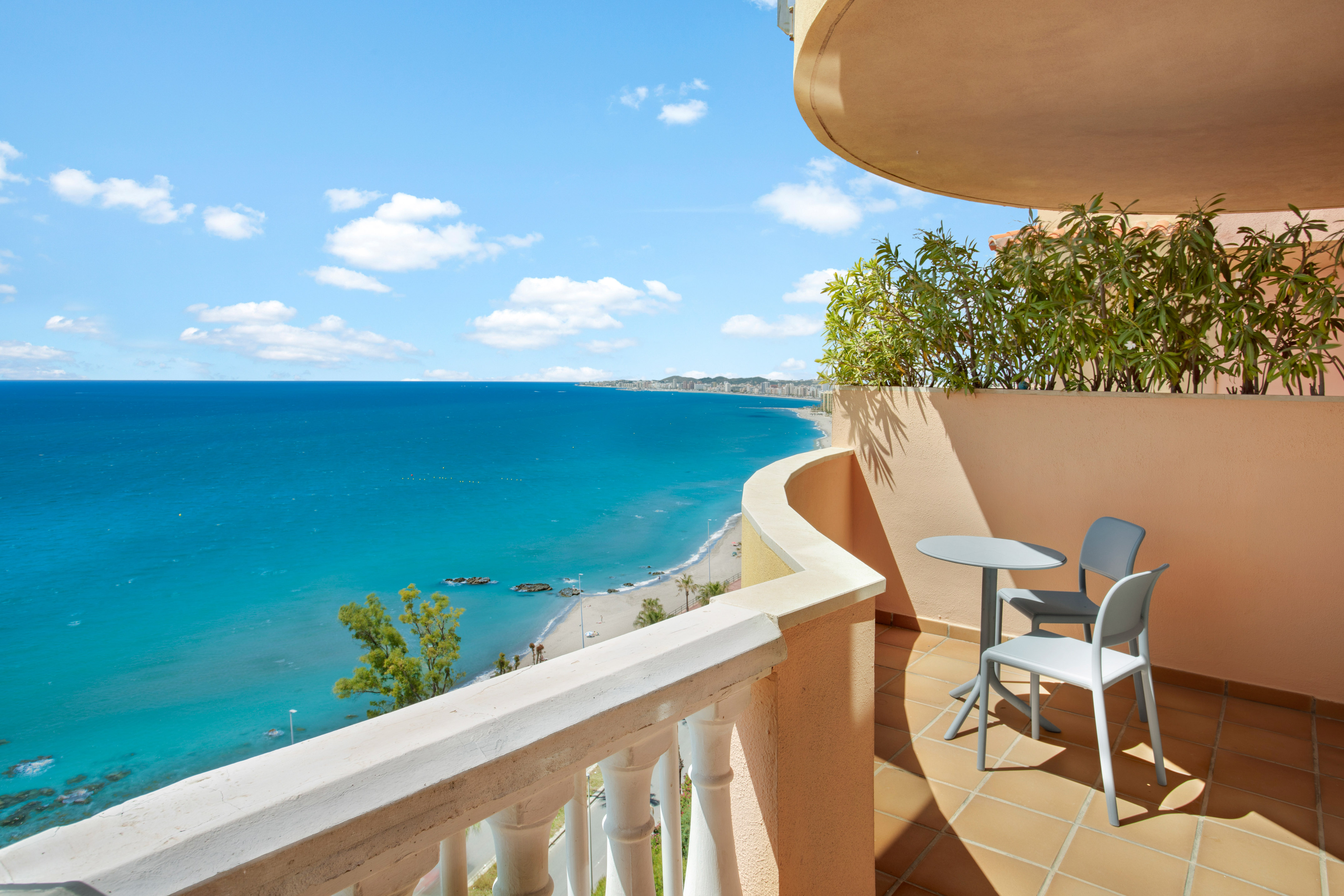 Balcony overlooking turquoise sea, sandy beach, and distant resort town.