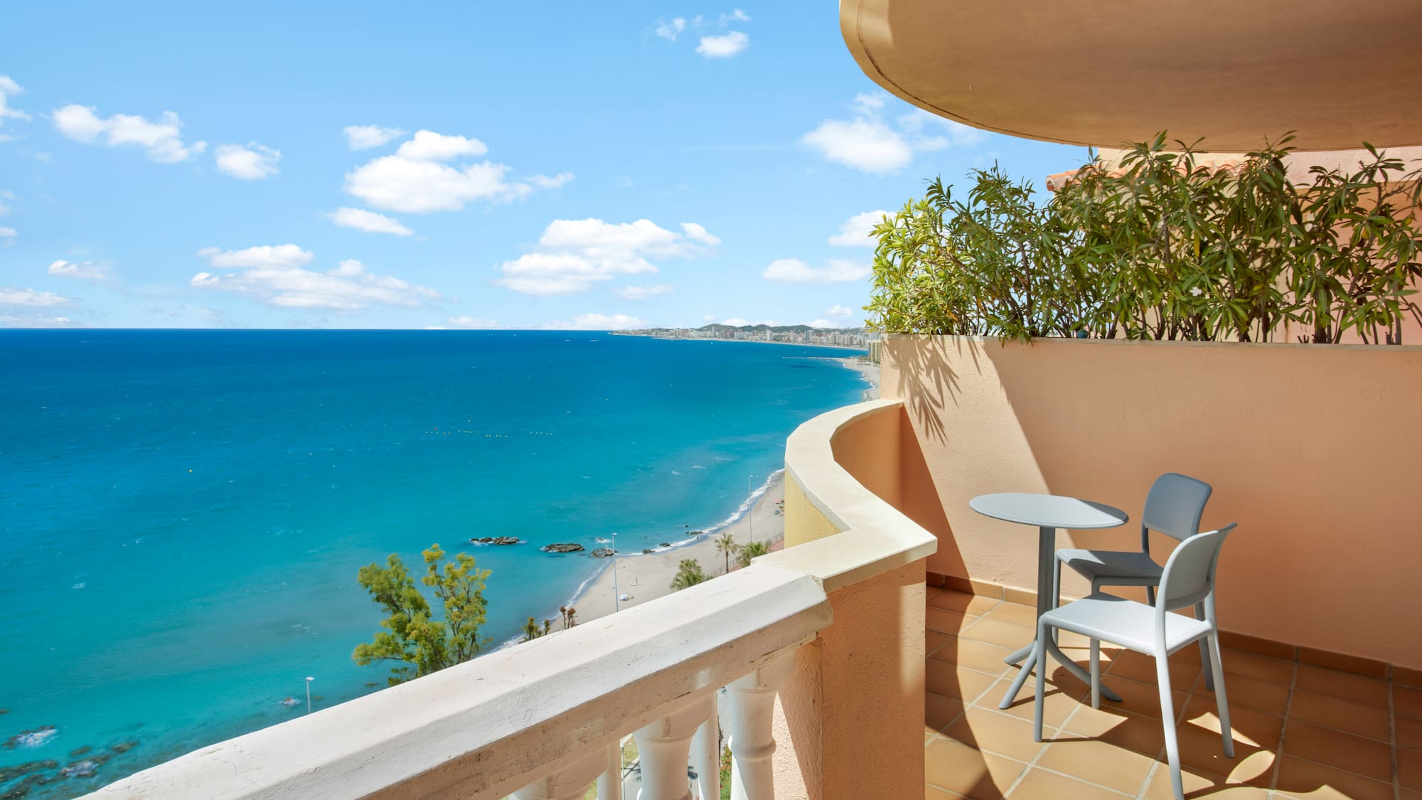 Balcony overlooking turquoise sea, sandy beach, and distant resort town.
