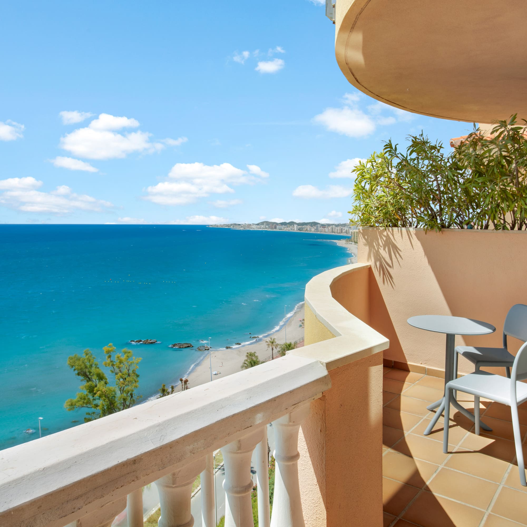 Balcony overlooking turquoise sea, sandy beach, and distant resort town.