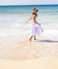 a woman in a white dress and hat walking in the water