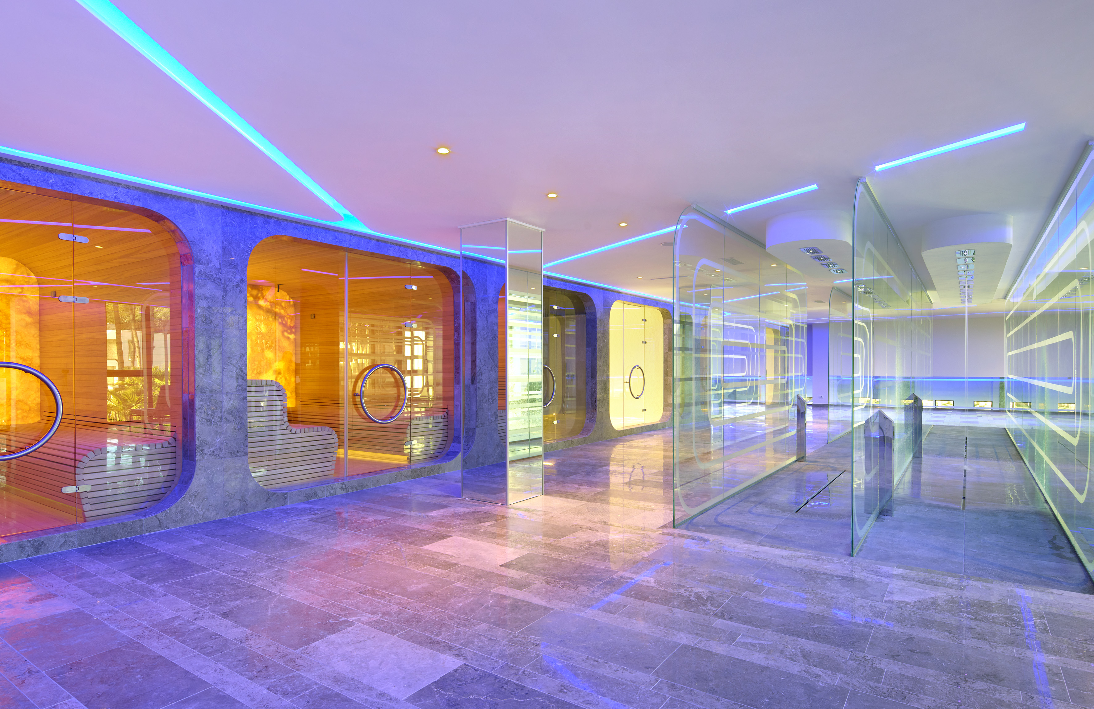 Modern spa interior with glass saunas, warm wood, and vibrant blue LED lighting.