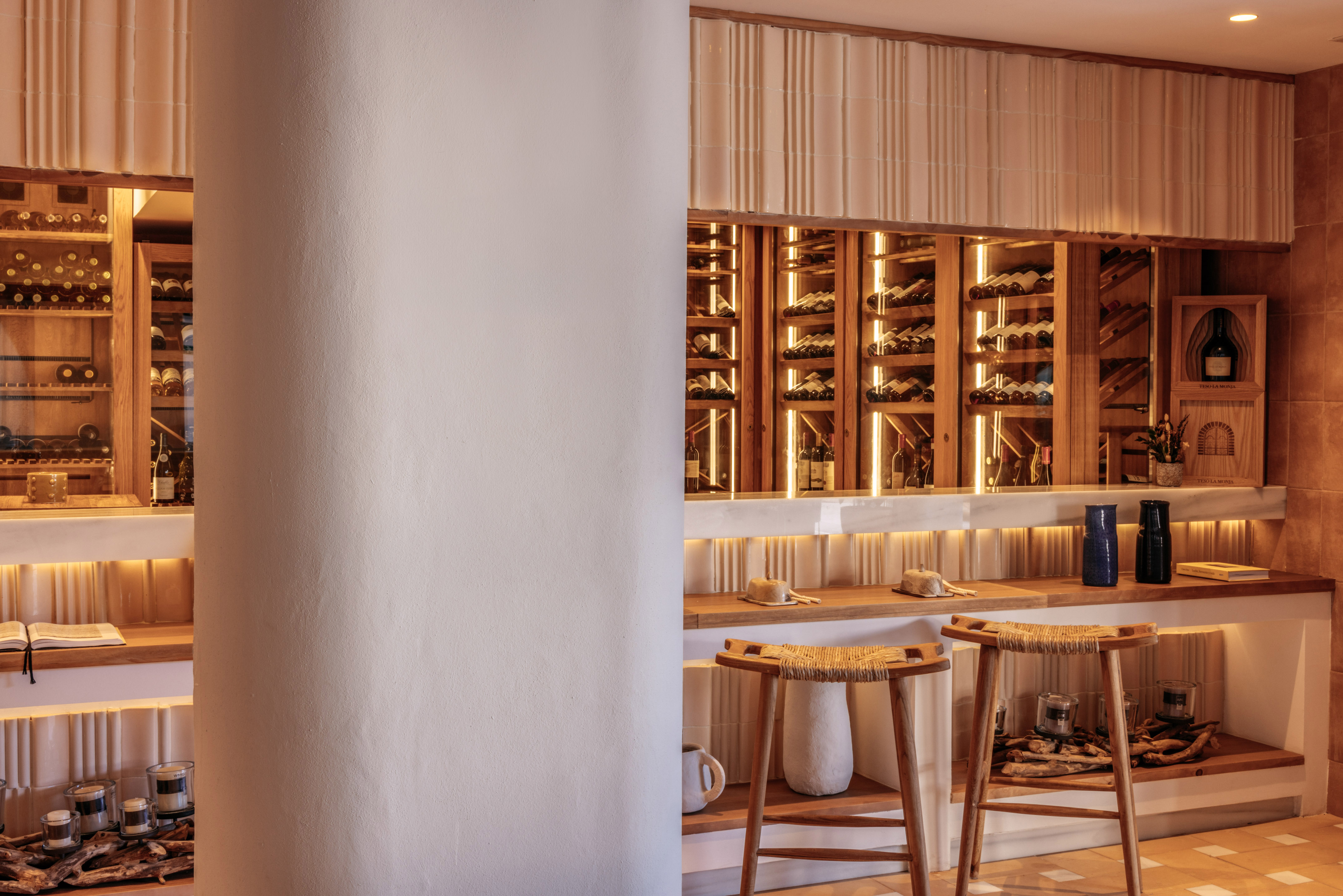 Modern wine cellar with illuminated bottles, wooden shelves, and bar stools.