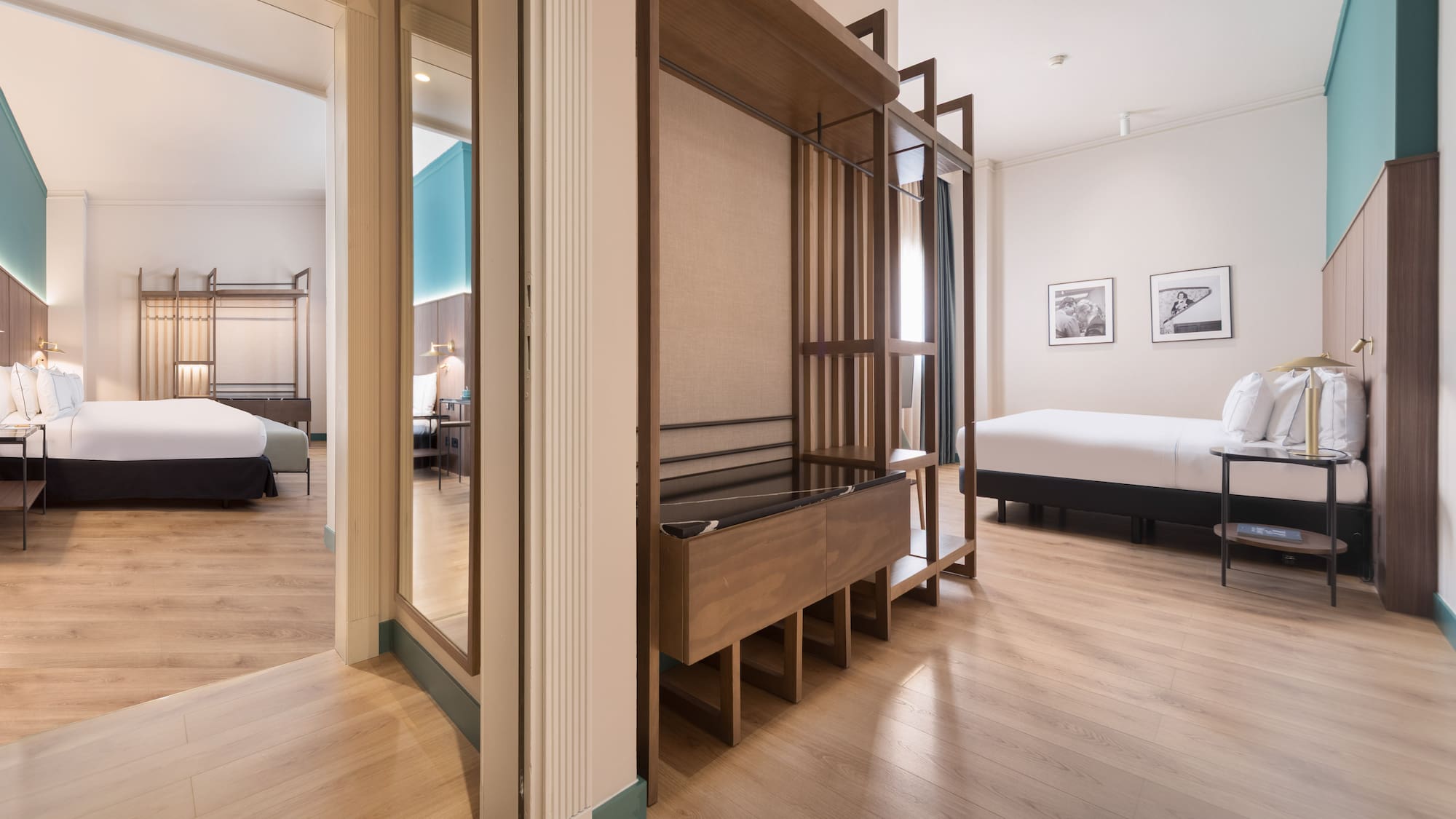 Modern hotel suite with two beds, wooden floor, and open wardrobe.
