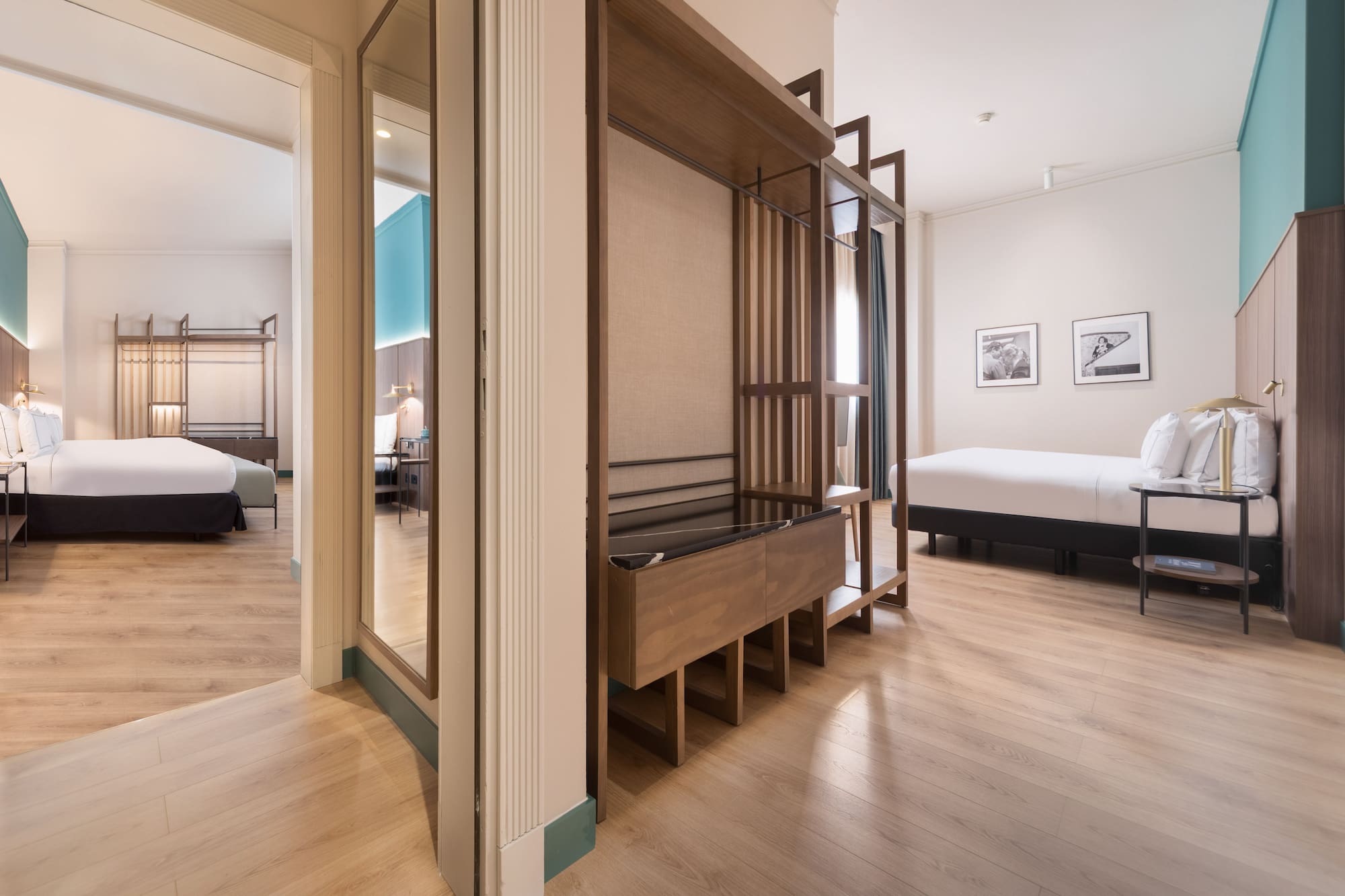 Modern hotel suite with two beds, wooden floor, and open wardrobe.