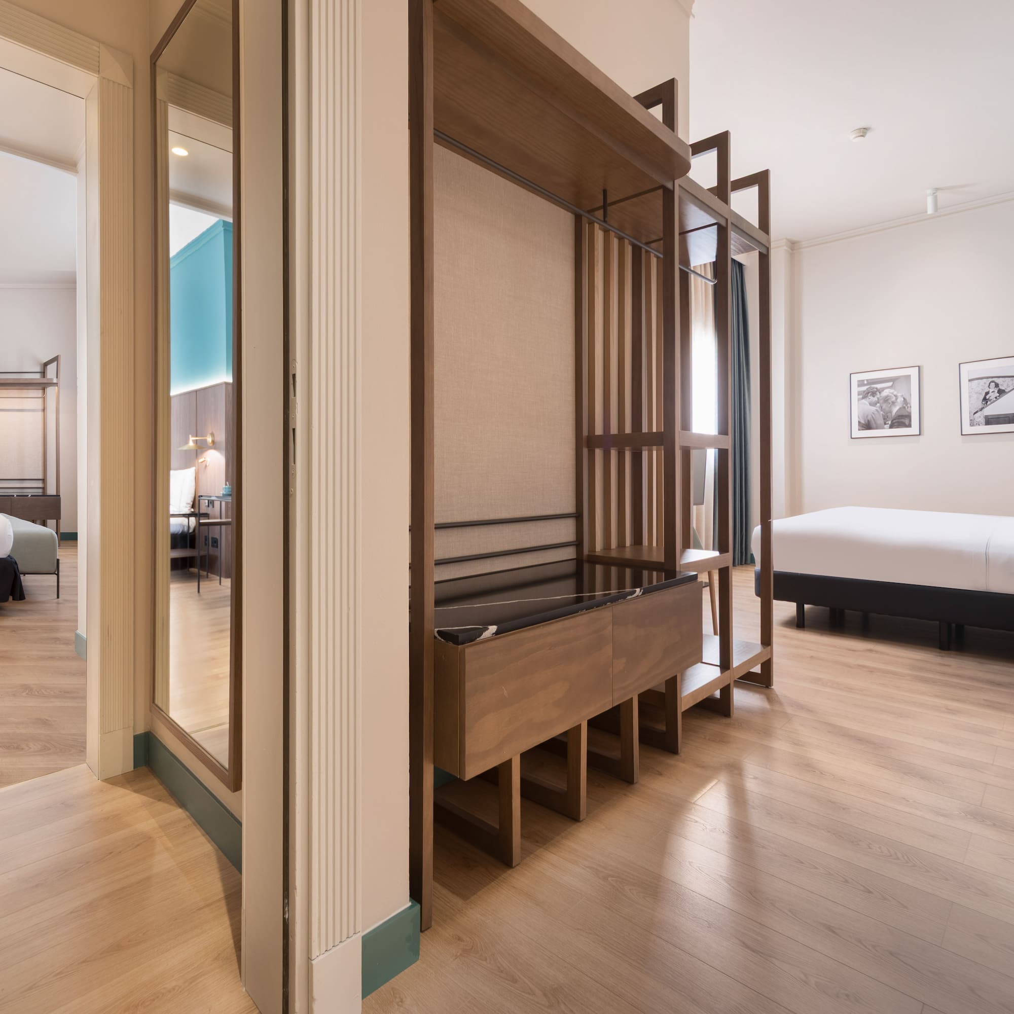 Modern hotel suite with two beds, wooden floor, and open wardrobe.