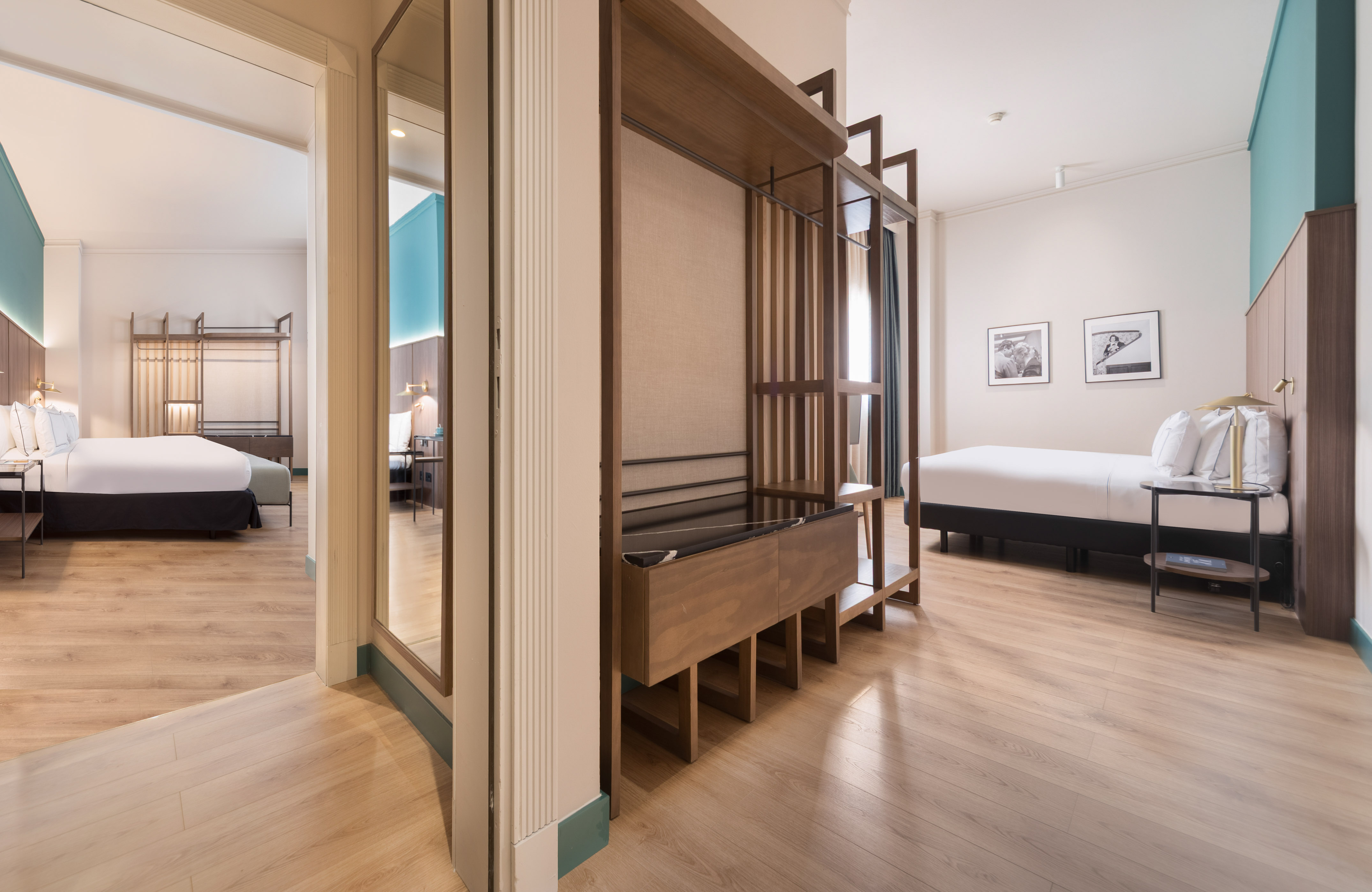 Modern hotel suite with two beds, wooden floor, and open wardrobe.