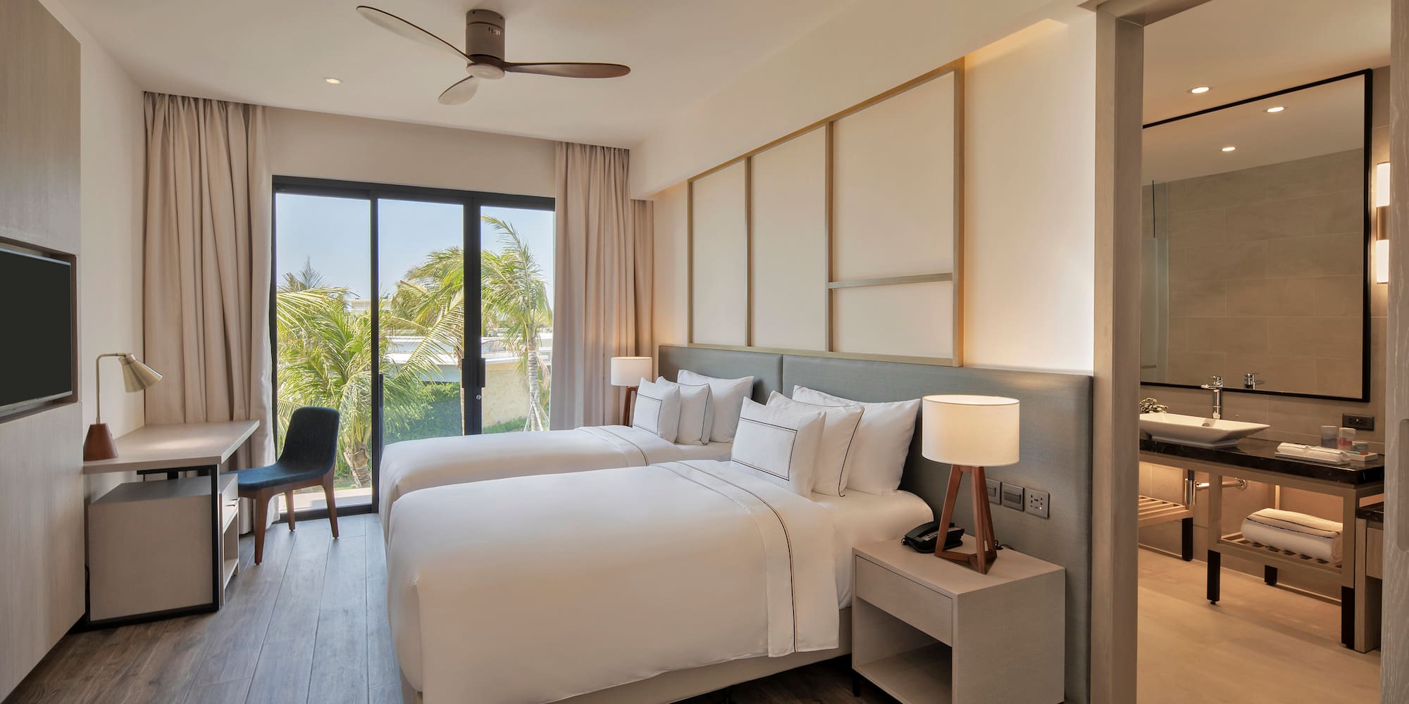 Modern hotel room with twin beds, tropical view, desk, and adjoining bathroom.