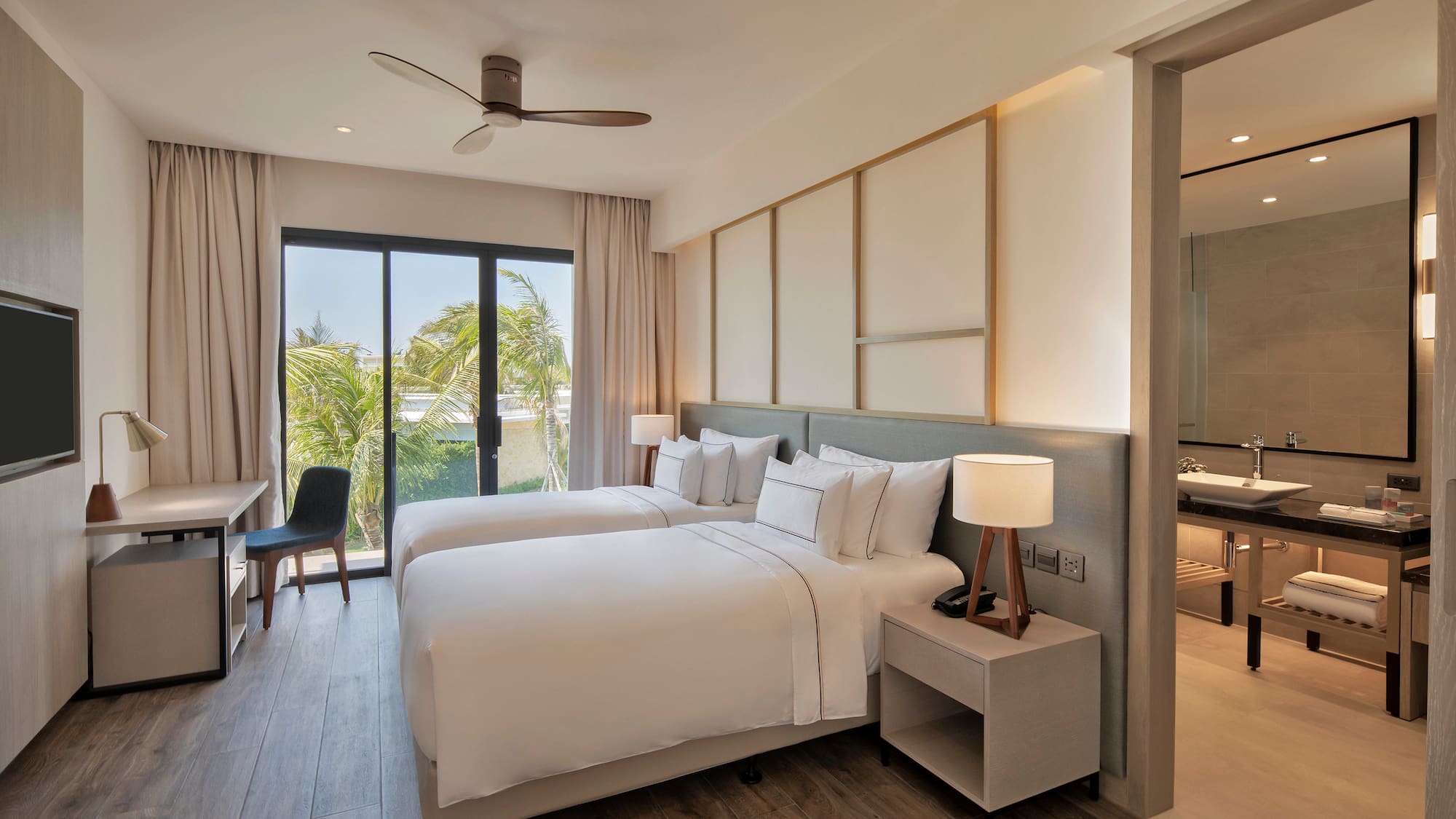 Modern hotel room with twin beds, tropical view, desk, and adjoining bathroom.