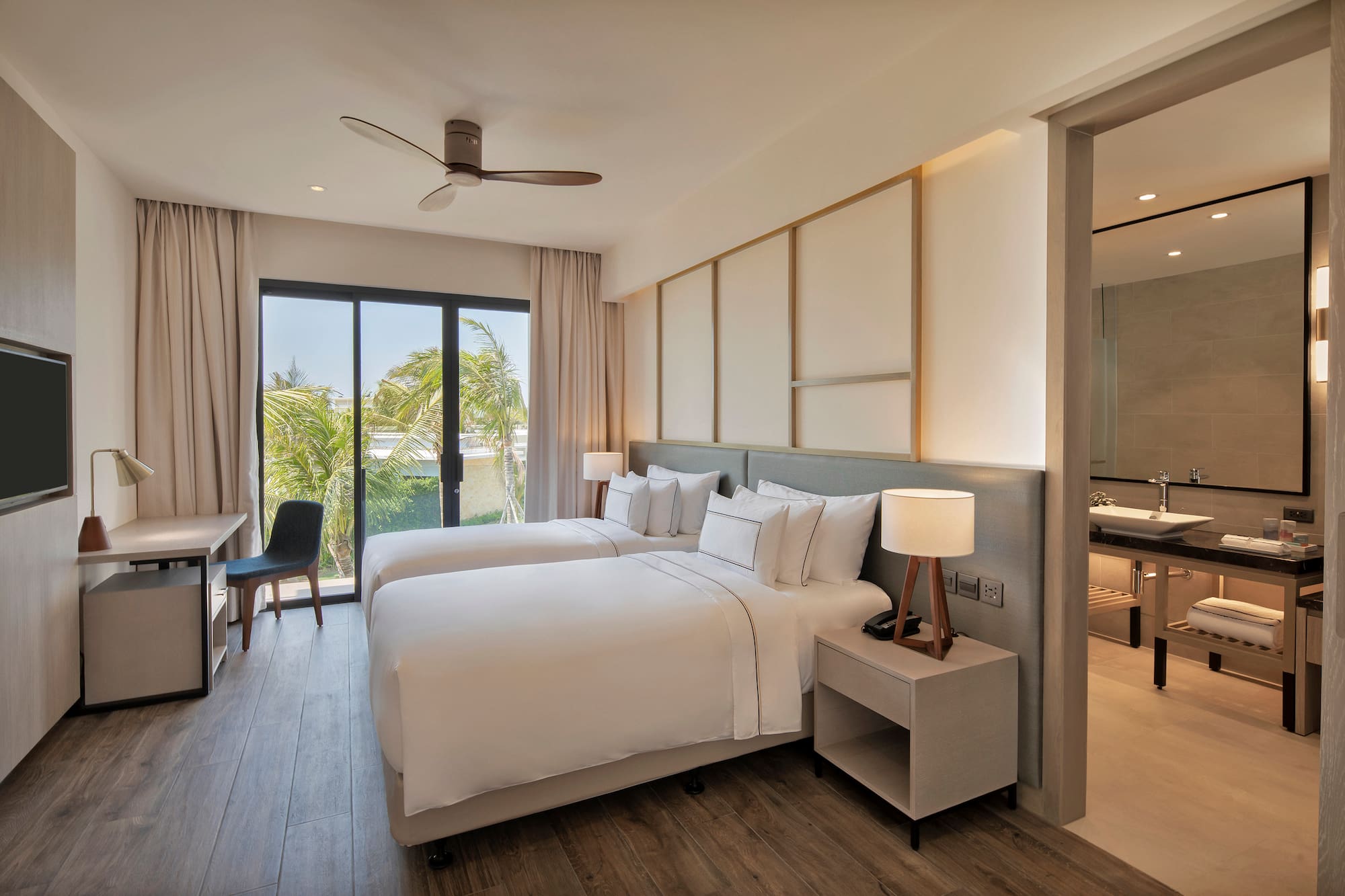 Modern hotel room with twin beds, tropical view, desk, and adjoining bathroom.