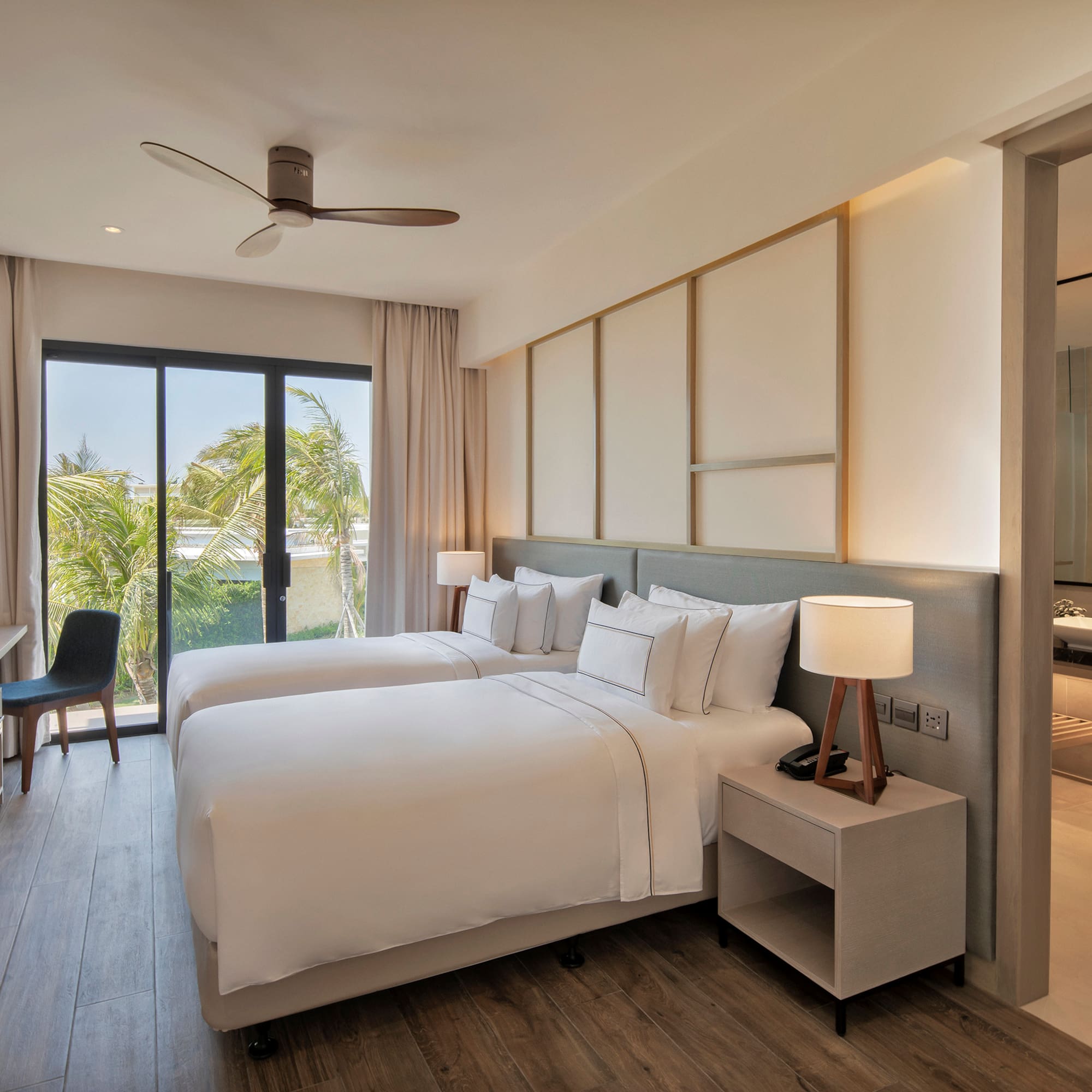 Modern hotel room with twin beds, tropical view, desk, and adjoining bathroom.