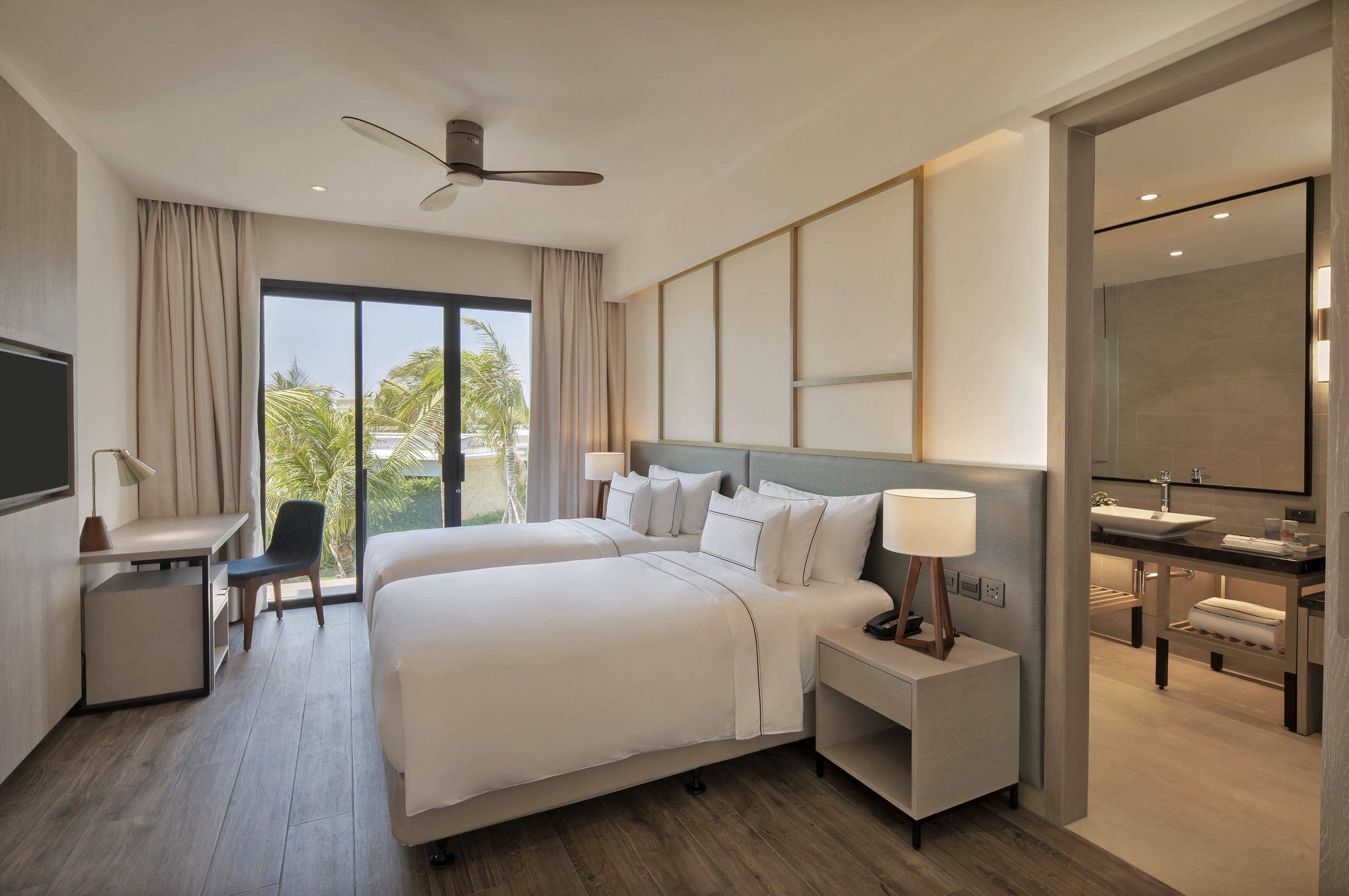 Modern hotel room with twin beds, tropical view, desk, and adjoining bathroom.