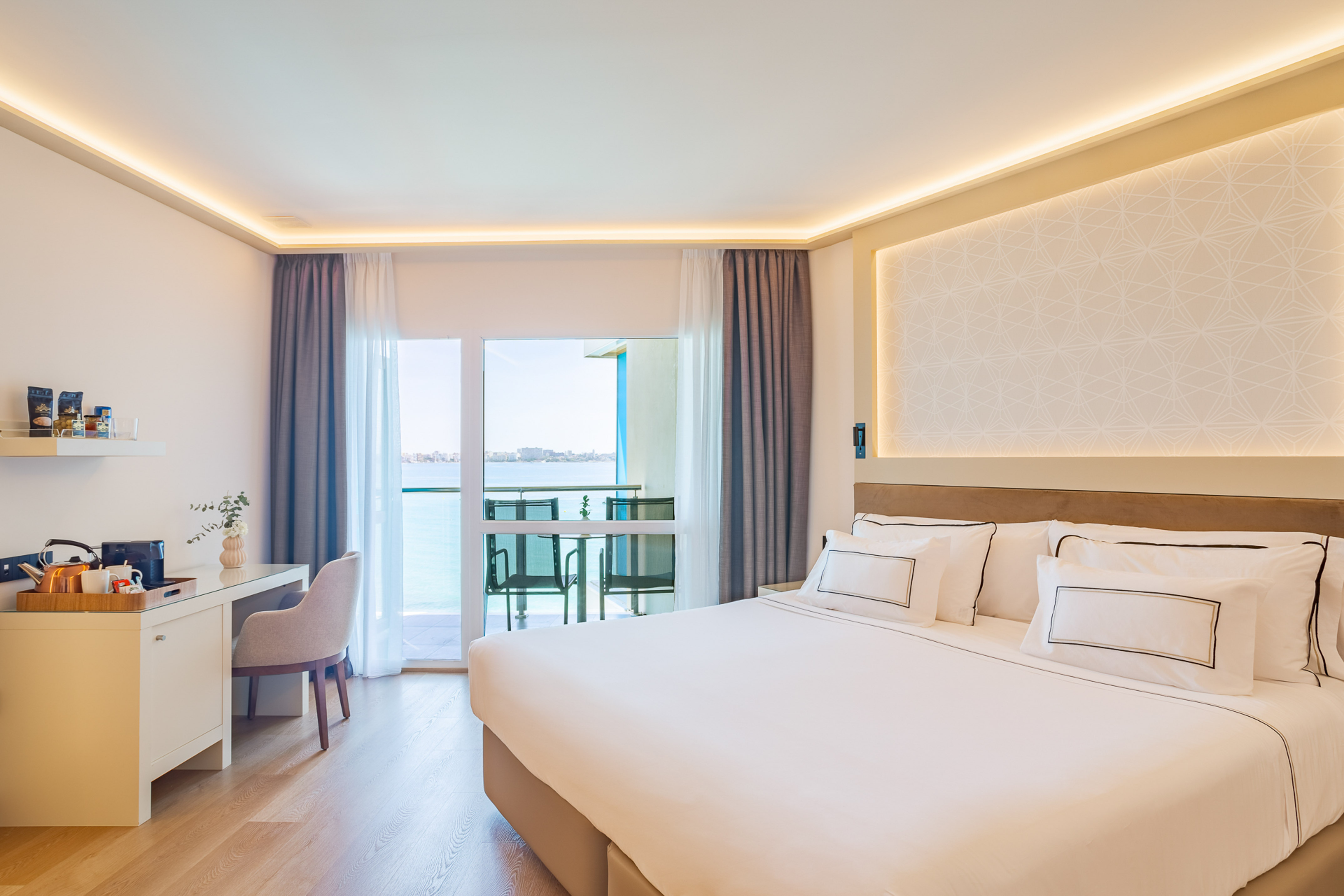 Luxury hotel room with sea view balcony, large bed, and modern decor.