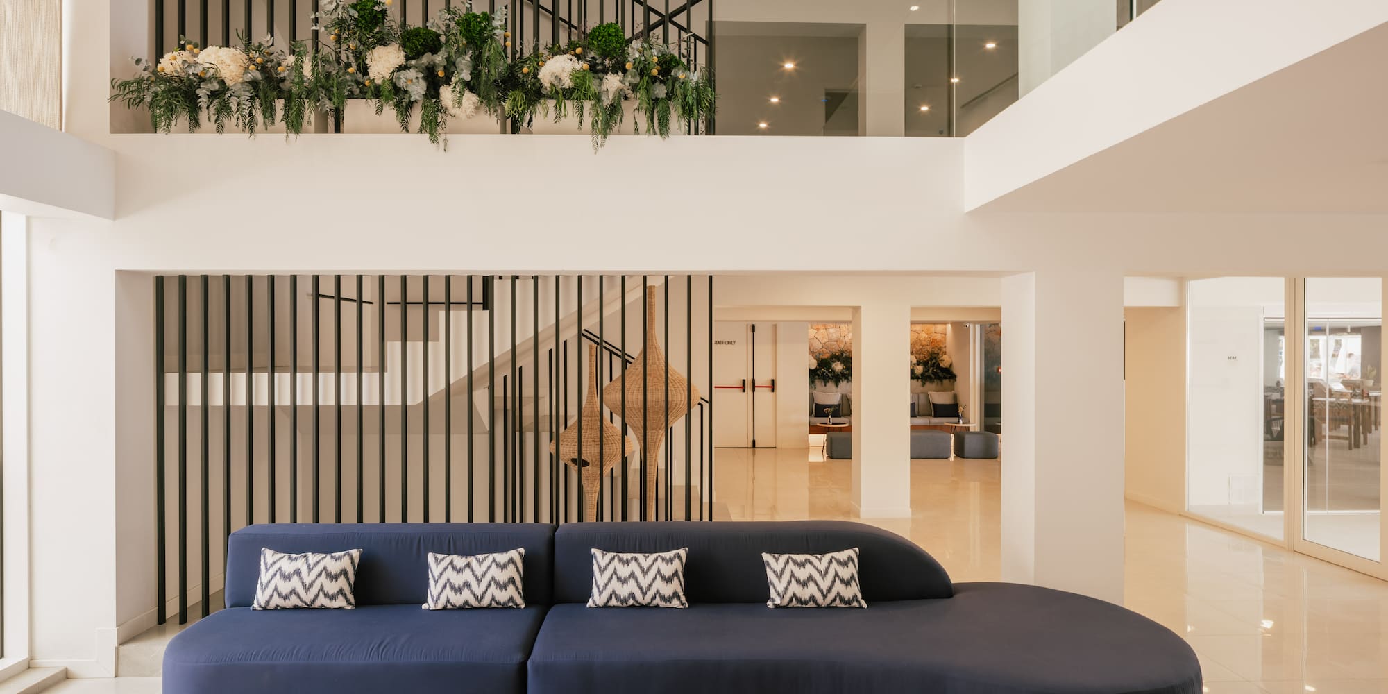 Lobby de hotel moderno con sofá azul, escalera de diseño y plantas.