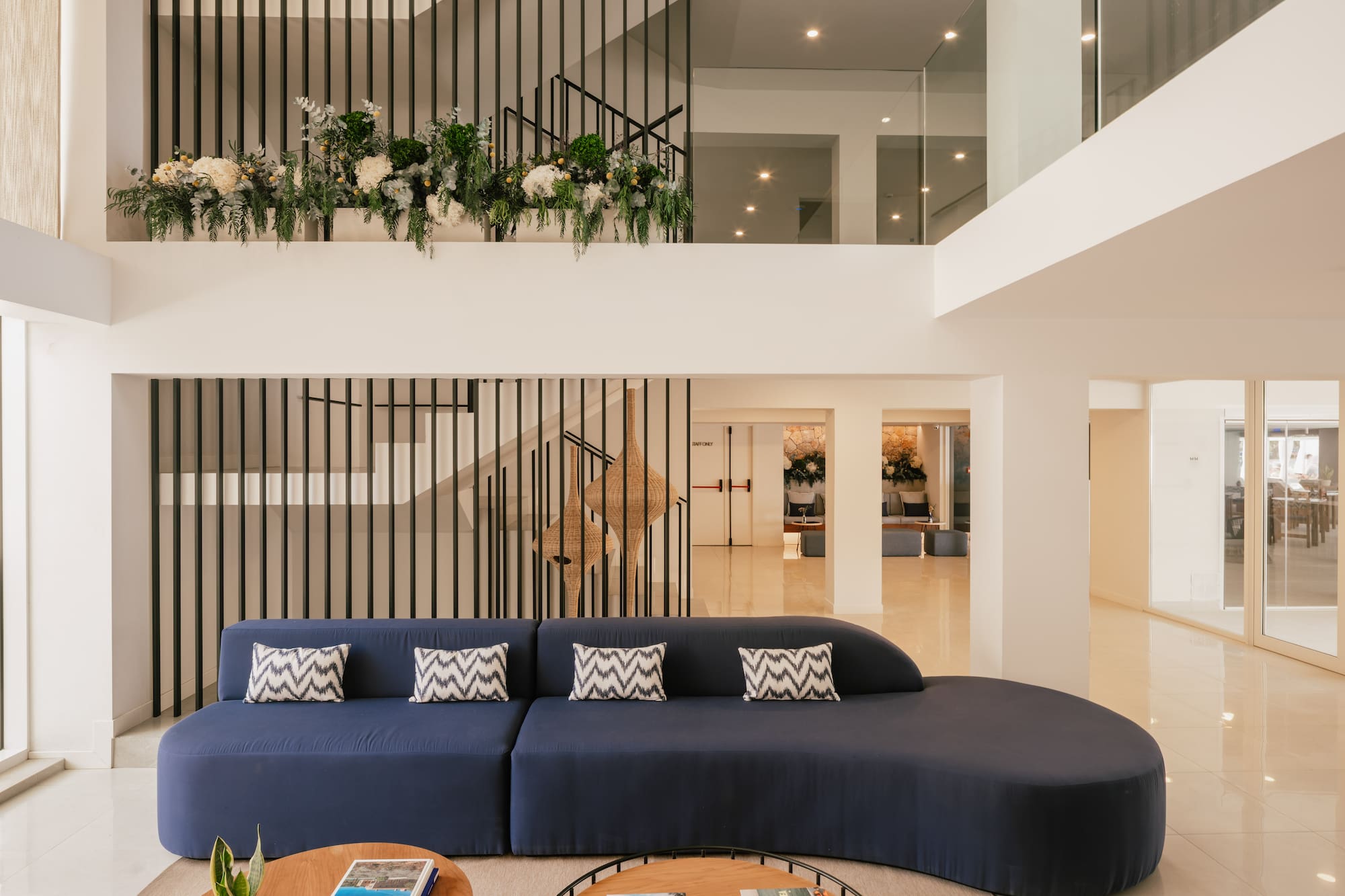 Lobby de hotel moderno con sofá azul, escalera de diseño y plantas.