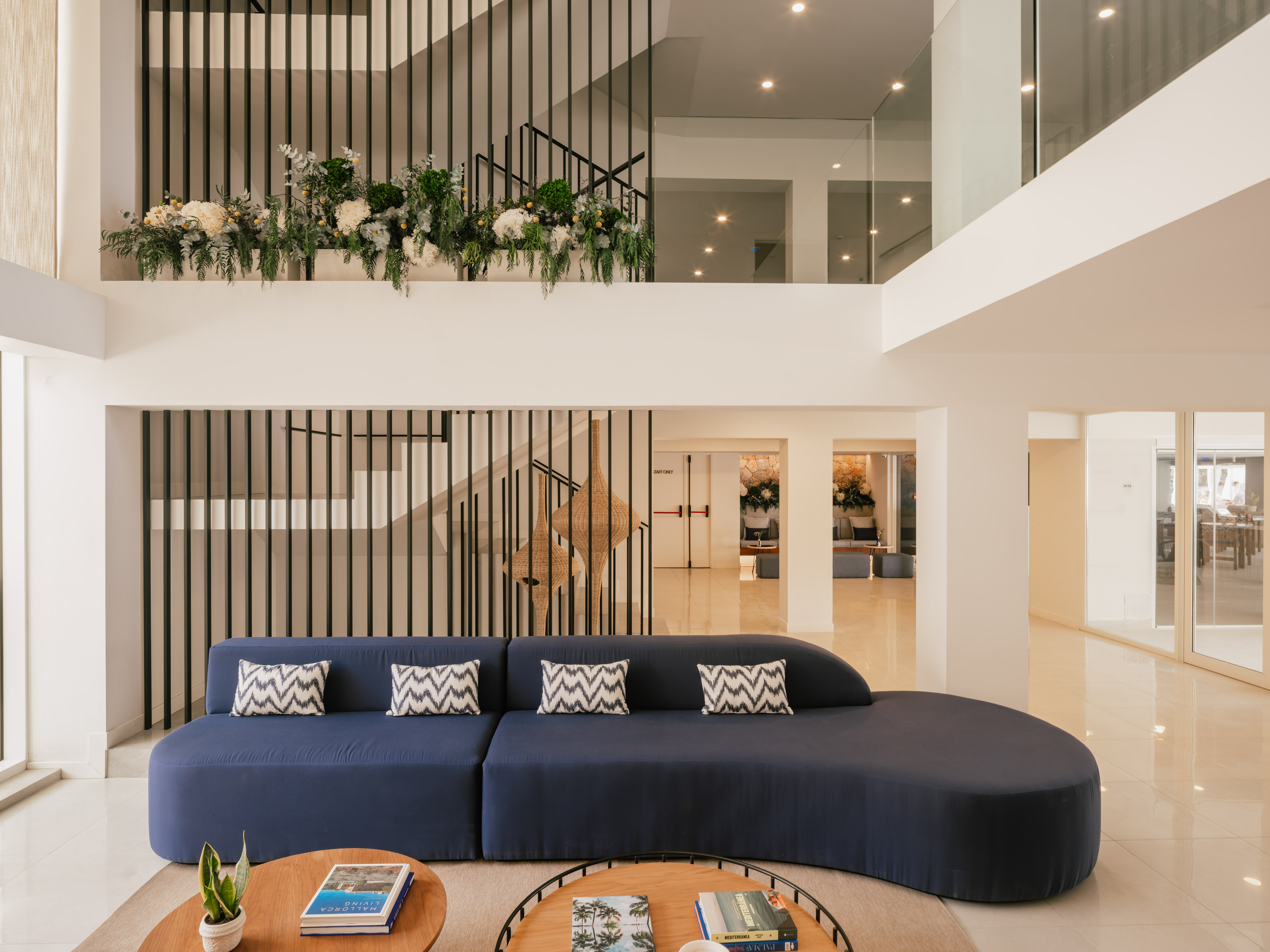 Lobby de hotel moderno con sofá azul, escalera de diseño y plantas.