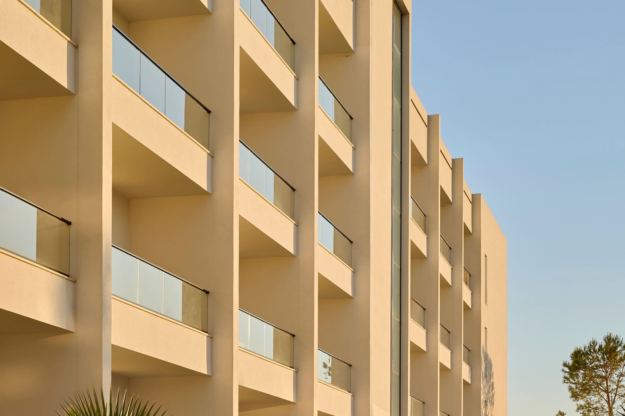 Cream-colored resort building with glass balconies and palm trees on a sunny day.