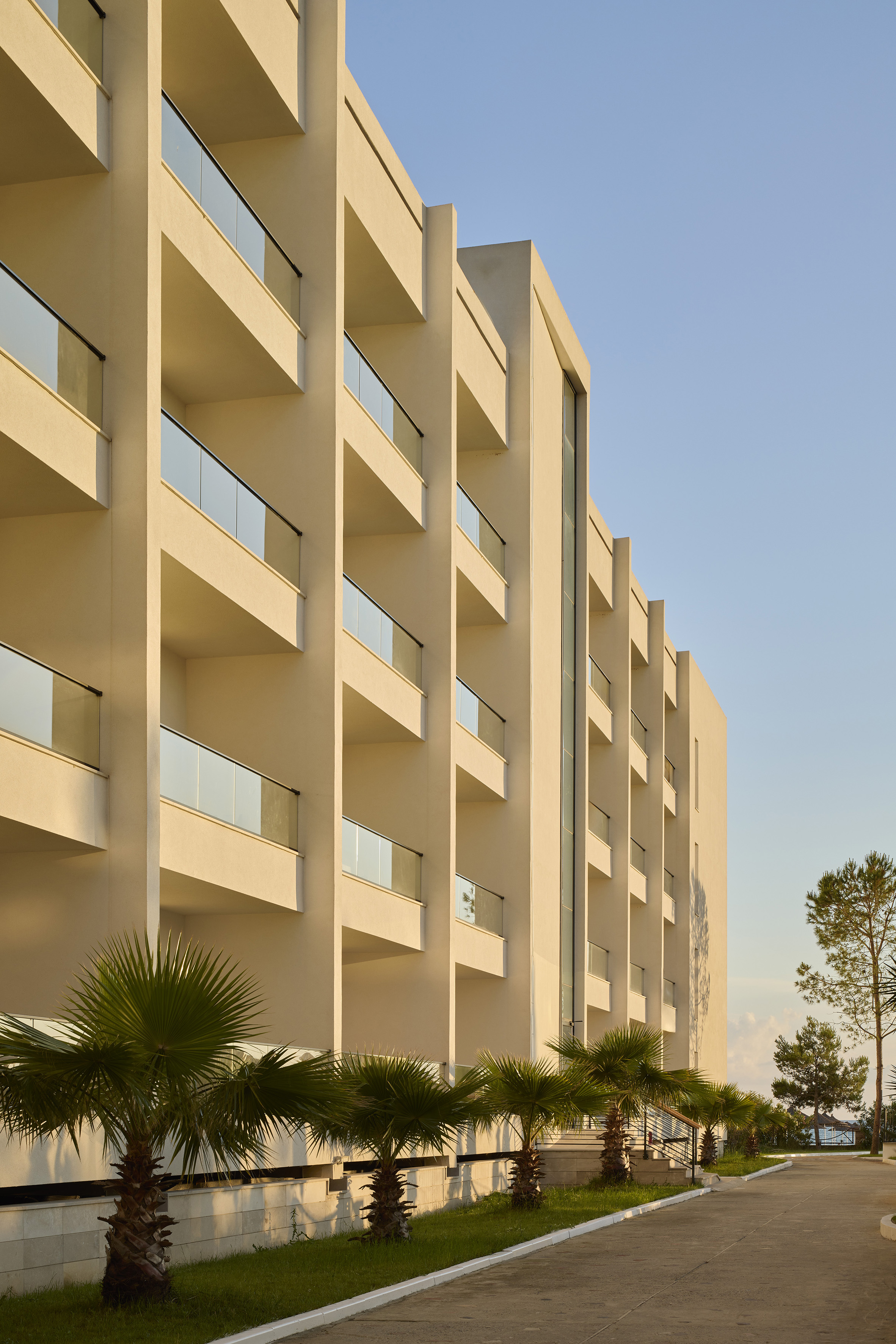 Cream-colored resort building with glass balconies and palm trees on a sunny day.