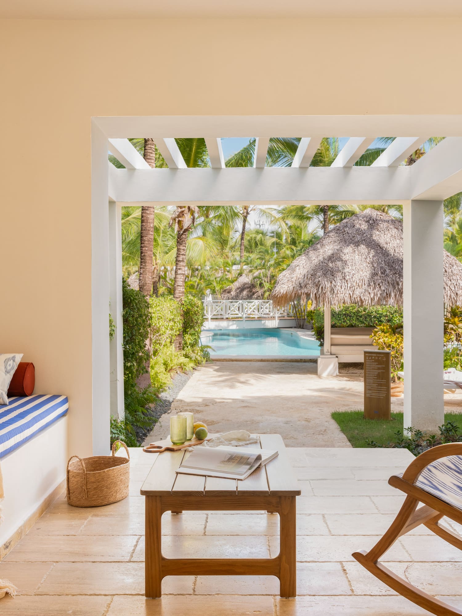 Tropical patio with pool view, palm trees, rocking chair, and cushioned bench.